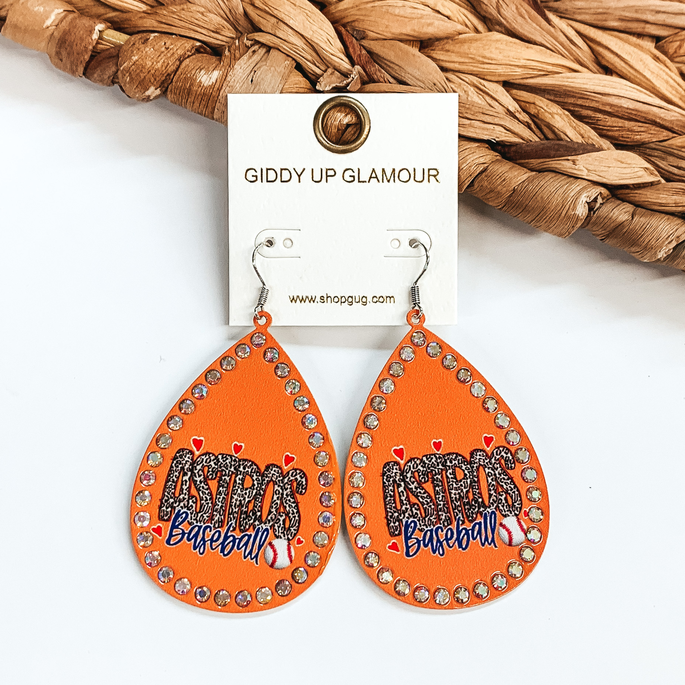 These are orange teardrop earrings with AB crystals  all around. It say's Astros in a leopard print with  red hearts and a baseball. These earrings are taken  on a white background and leaned up against a  brown woven slate.
