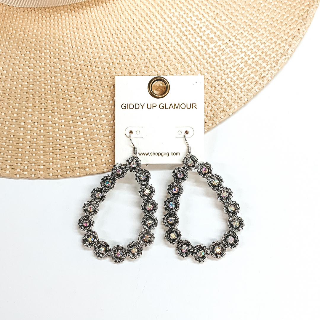 Silver, open teardrop outline earrings. These  earrings  have tiny, engraved flowers that make out the shape  of a teardrop. The middle of each flower has an AB  crystal. These earrings are pictured laying on a  straw hat brim and a white background.