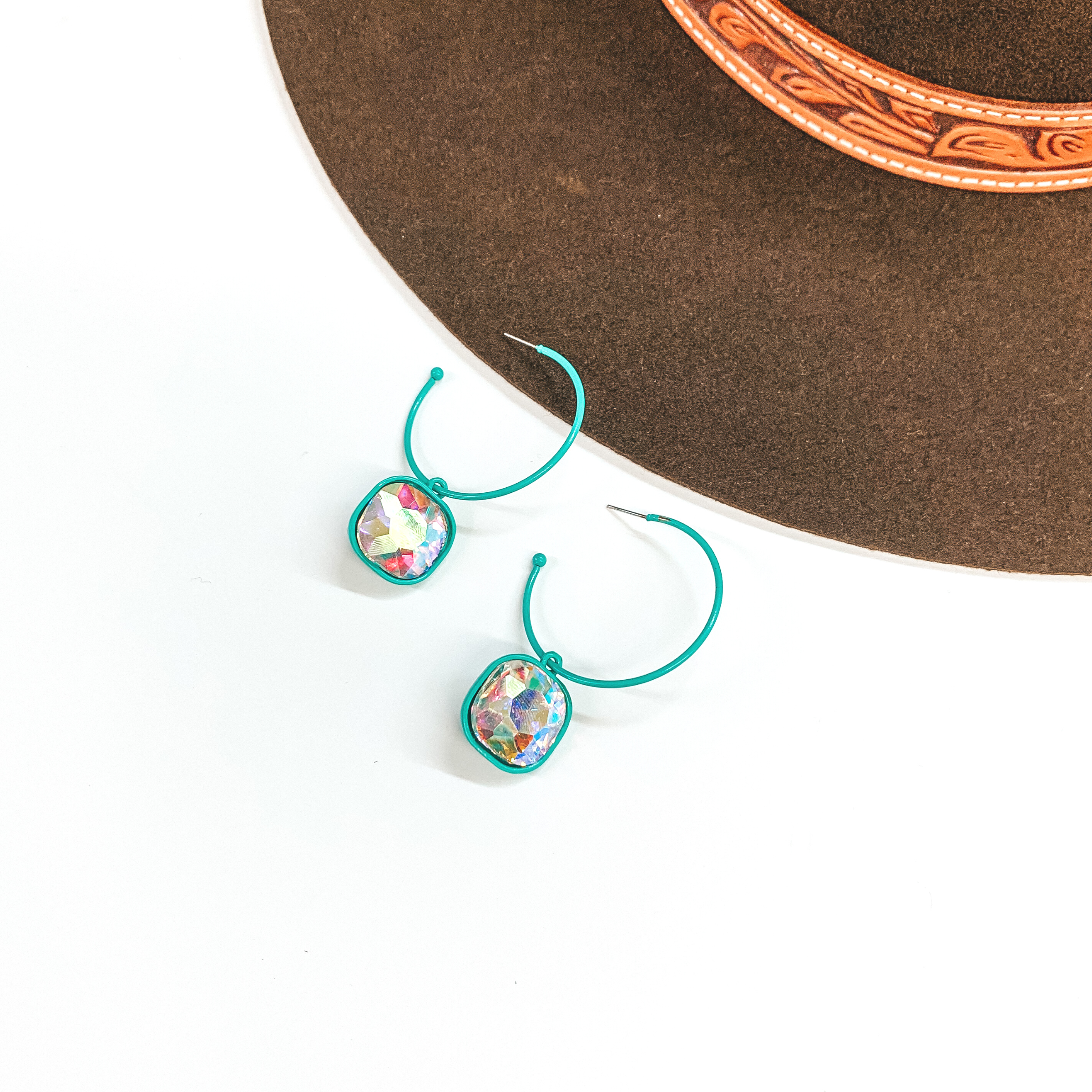 These are turquoise open ended hoop earrings with  a cushion cut AB crystal hanging pendant. These  earrings are taken on a white background and a dark  brown hat in the back as decor.