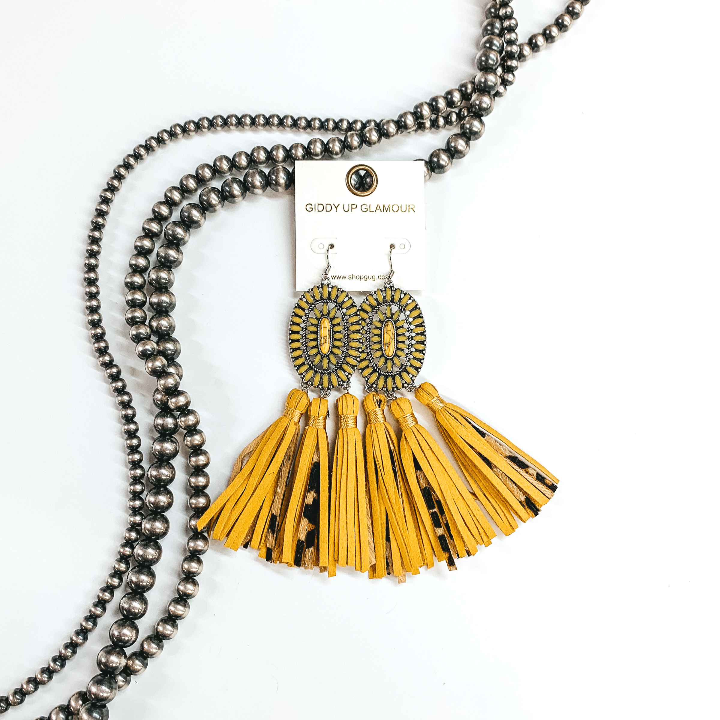 Yellow stone oval cluster earrings in a silver settings with three  faux leather tassels in yellow and leopard print. These earrings are taken  on a white background and with Navajo pearls in the back as decor.