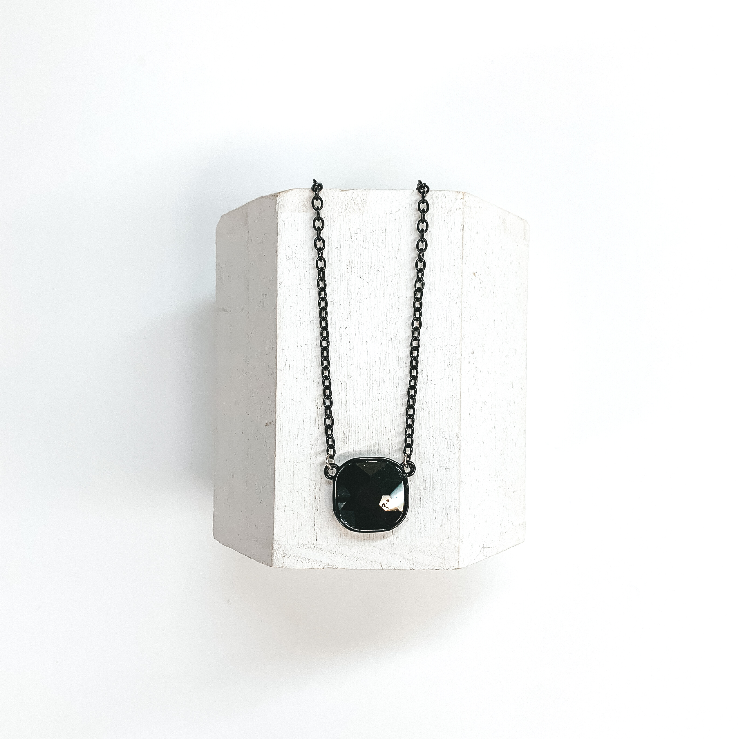 This is a black chain necklace with a black cushion cut crystal pendant.  This necklace is taken on a white block and on a white background.