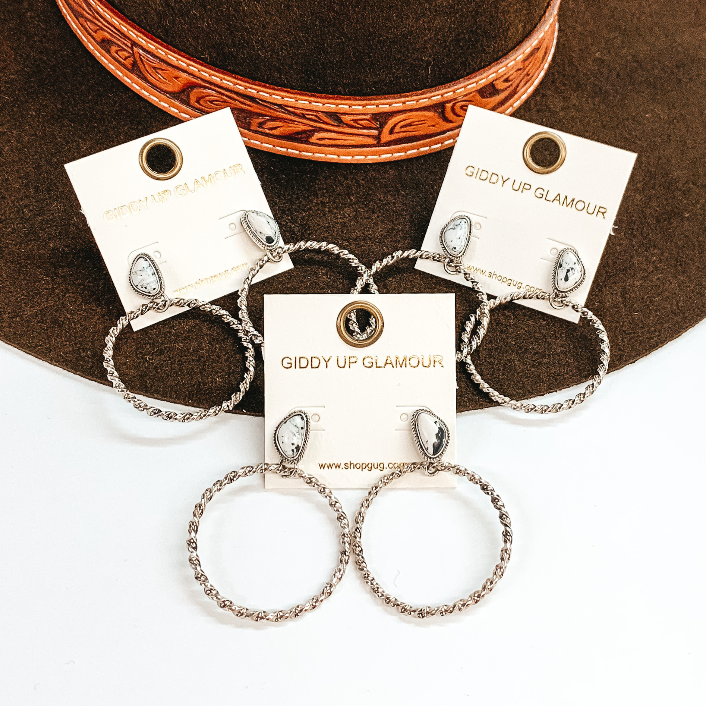 These are three pairs of silver circle drop earrings with an asymmetrical  white and black mix stone post backing. The circle drop has a twisted  rope texture in silver. These earrings are taken laying on  a dark brown hat brim  and on a white background.