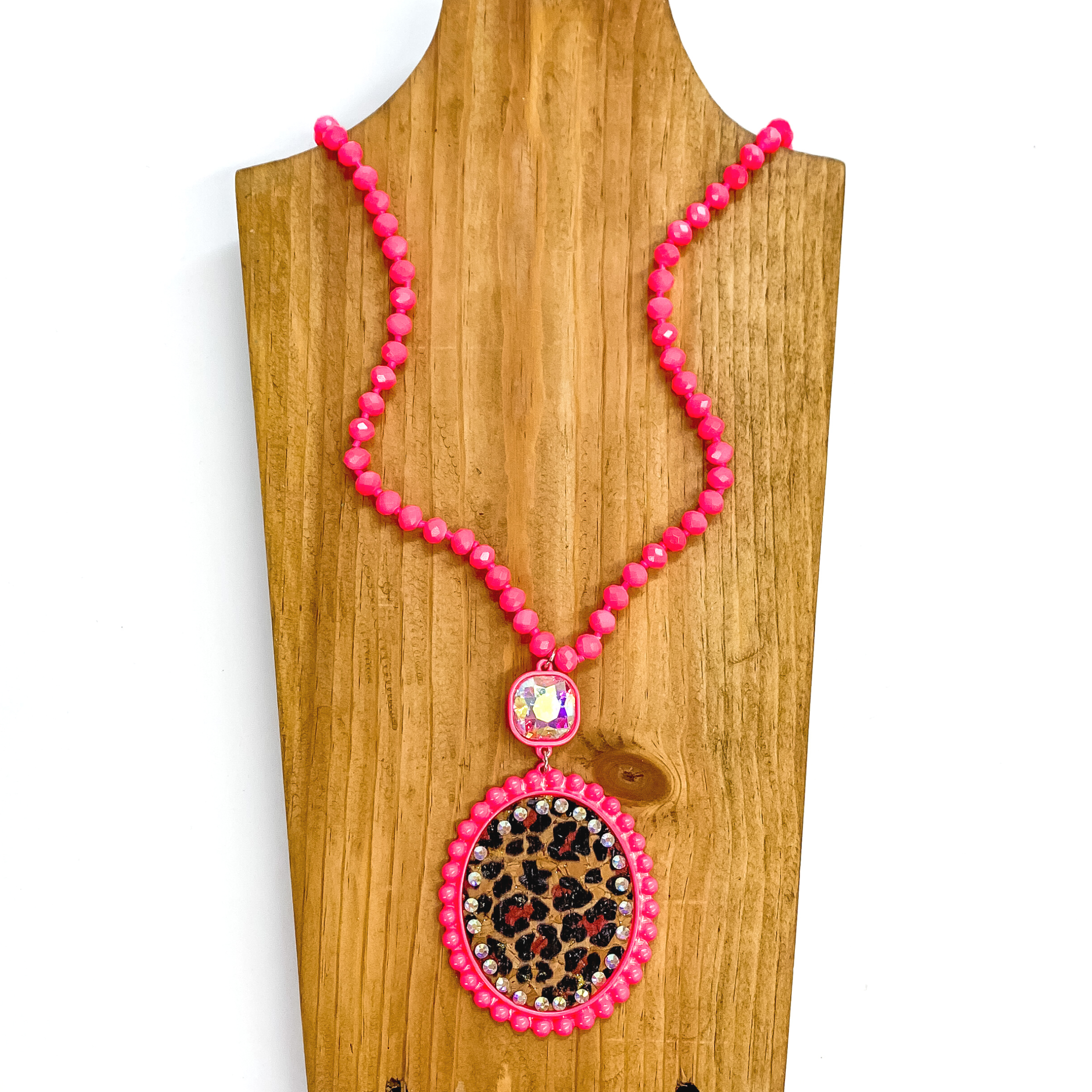 Long crystal beaded necklace in neon pink with a leopard print pendant  and AB cushion cut crystal connector. The pendant is in a neon pink setting,  the leopard print is on a cork material and has small AB crystals all  around. This necklace is taken laying on a brown necklace board and white  background.