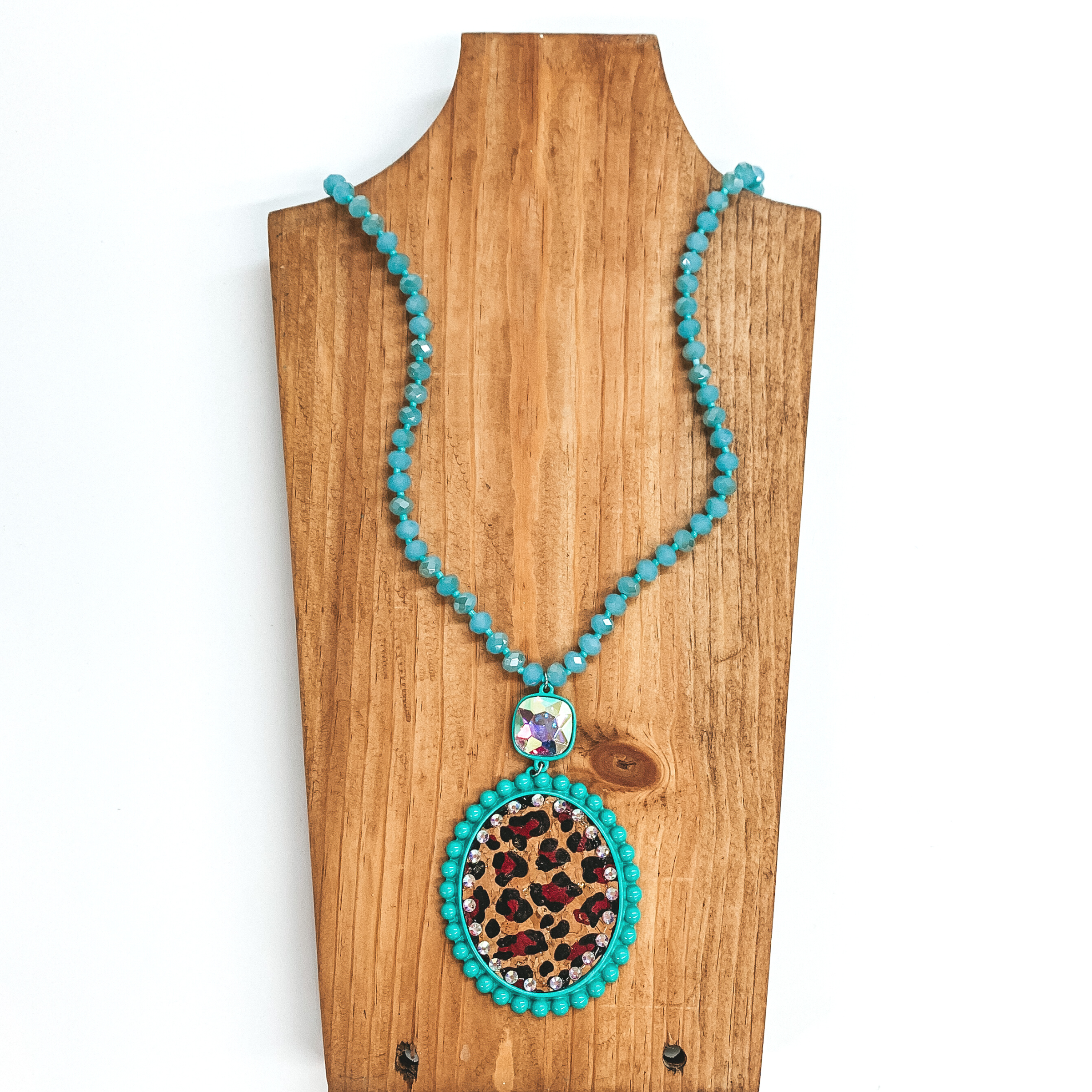 Long crystal beaded necklace in turquoise with a leopard print pendant  and AB cushion cut crystal connector. The pendant is in a turquoise setting,  the leopard print is on a cork material and has small AB crystals all  around. This necklace is taken laying on a brown necklace board and white  background.