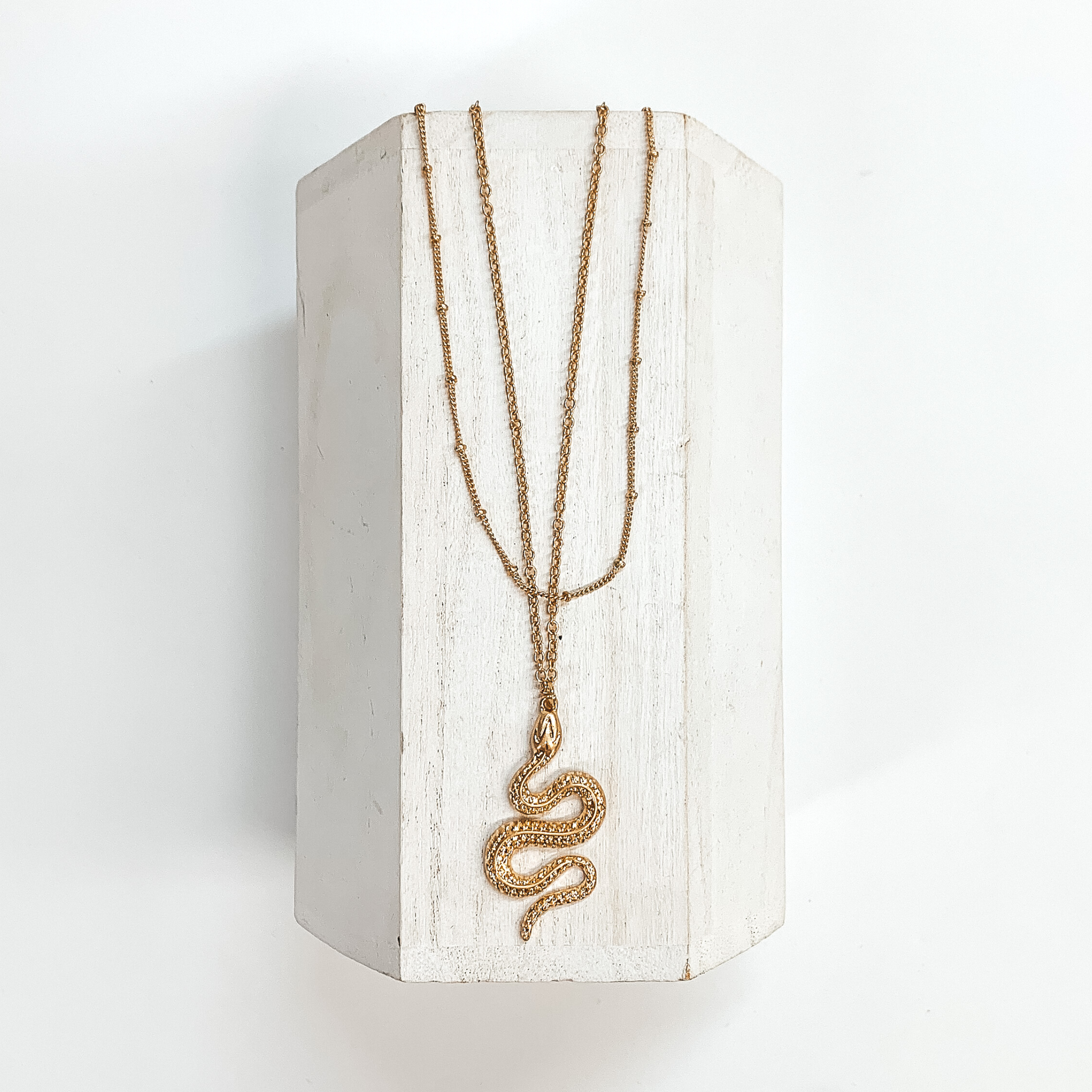 Double layered gold necklaces with a large snake pendant, the smallest  chain has spacers throughout. This necklace is taken on a white block  and a white background.