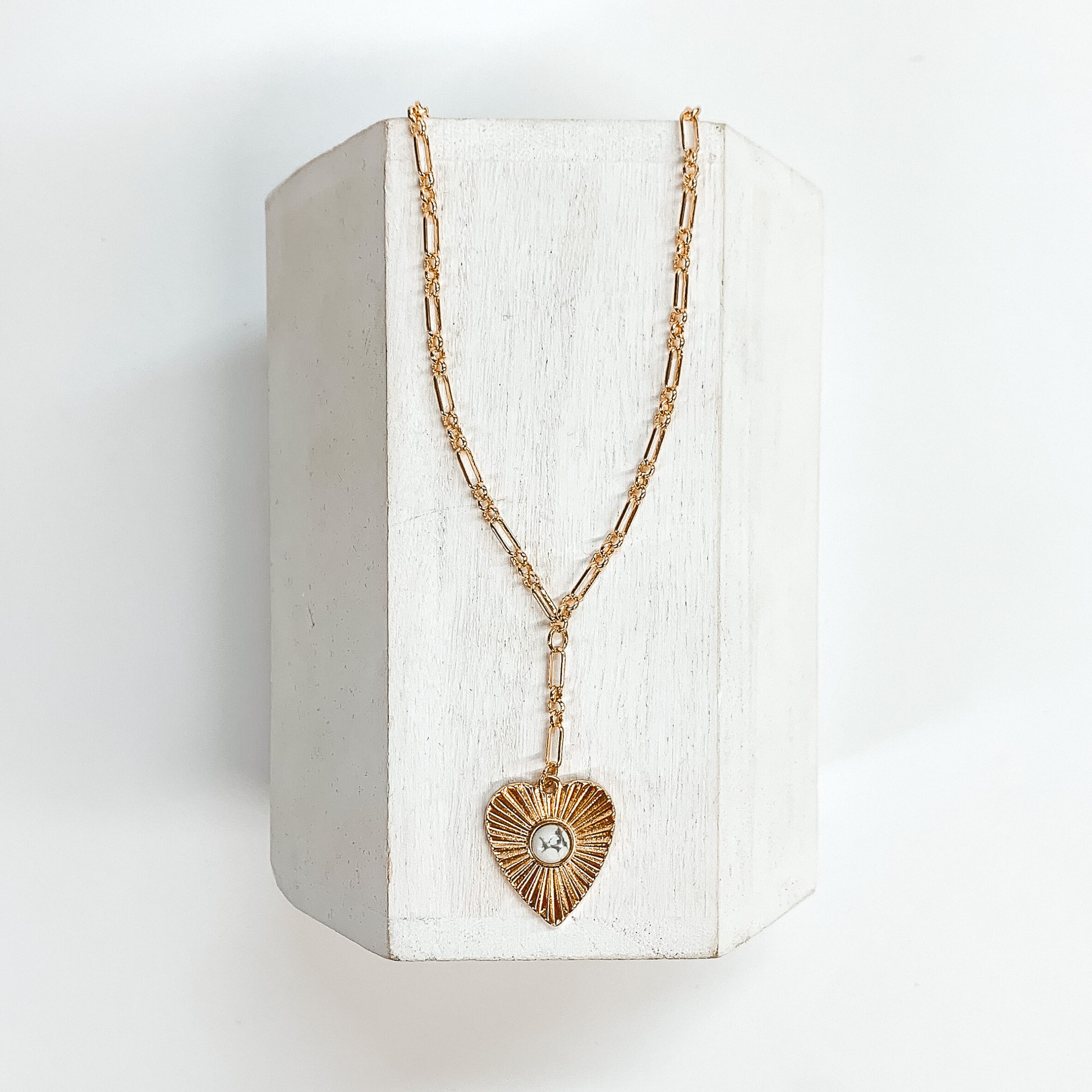 Gold linked chain with a sunburst heart pendant with a small white stone  in the center. This necklace is taken on a white block and on a white  background.