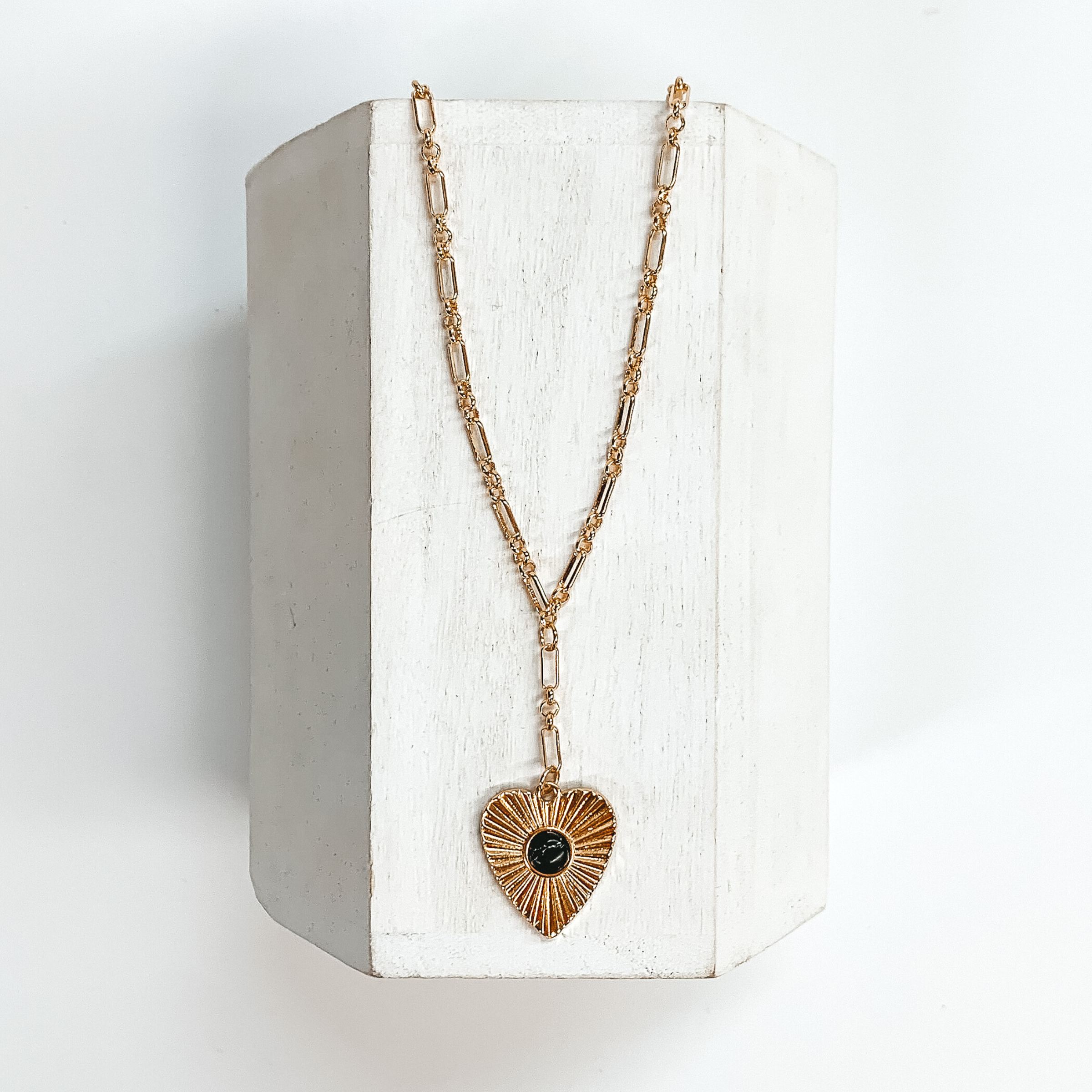 Gold linked chain with a sunburst heart pendant with a small black stone  in the center. This necklace is taken on a white block and on a white  background.