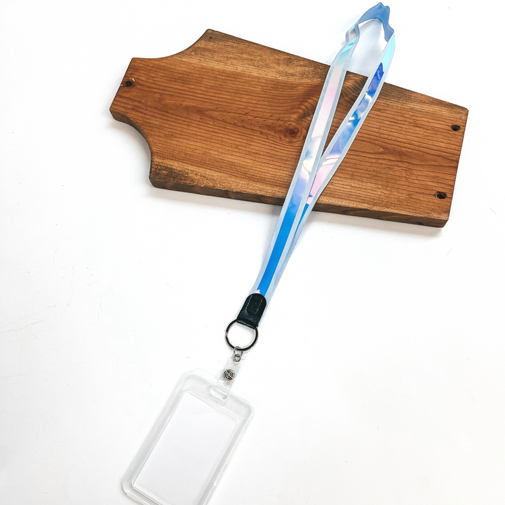 Periwinkle ribbon lanyard with holographic center and clear ID holder, this  lanyard is laying on a brown necklace holder and on a white background.