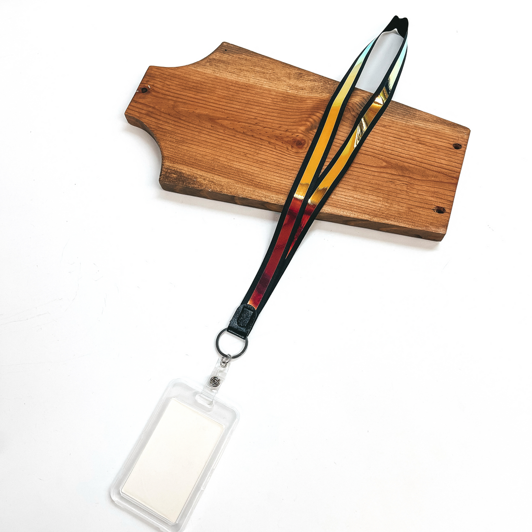 Black ribbon lanyard with holographic center and clear ID holder, this  lanyard is laying on a brown necklace holder and on a white background.