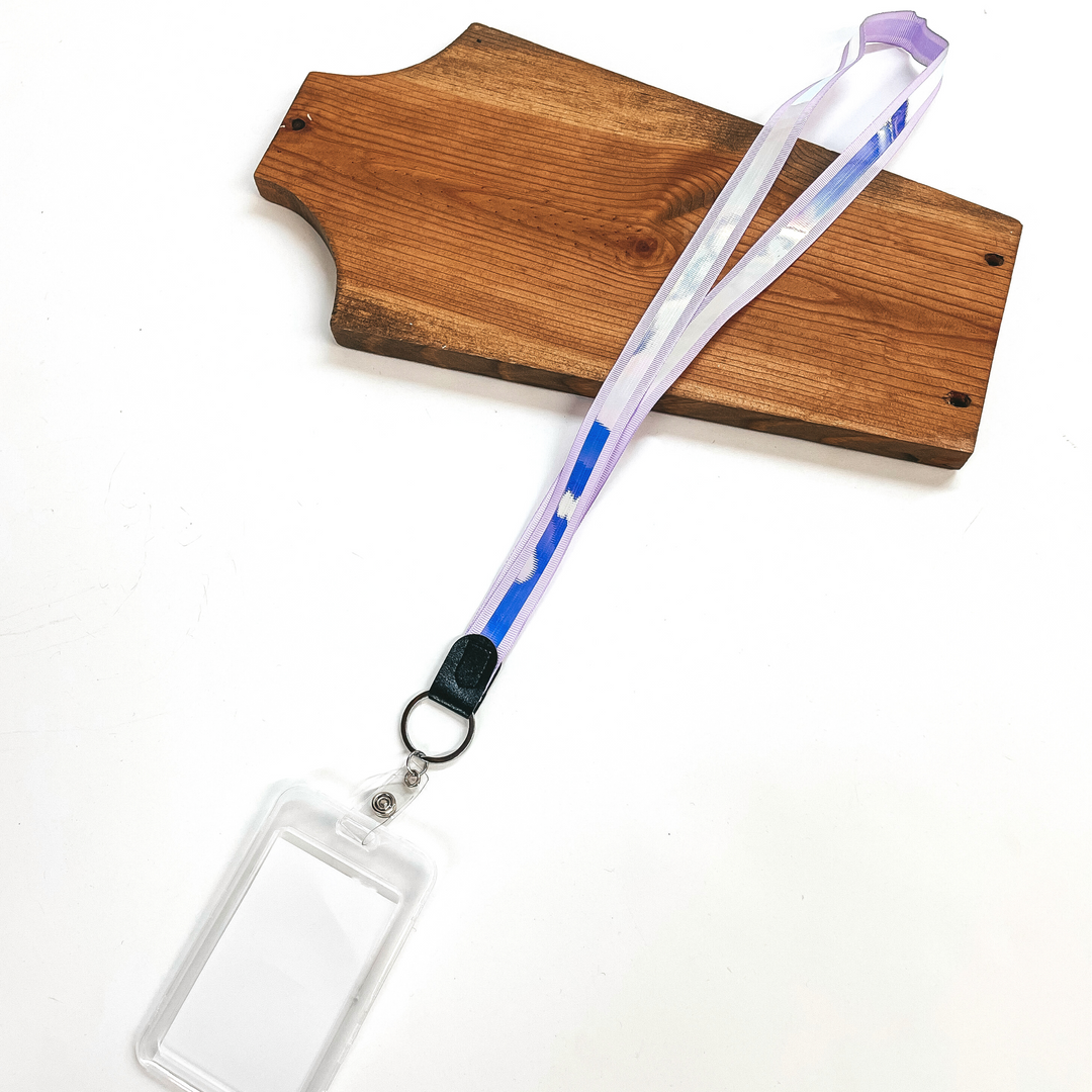 Lilac ribbon lanyard with holographic center and clear ID holder, this  lanyard is laying on a brown necklace holder and on a white background.