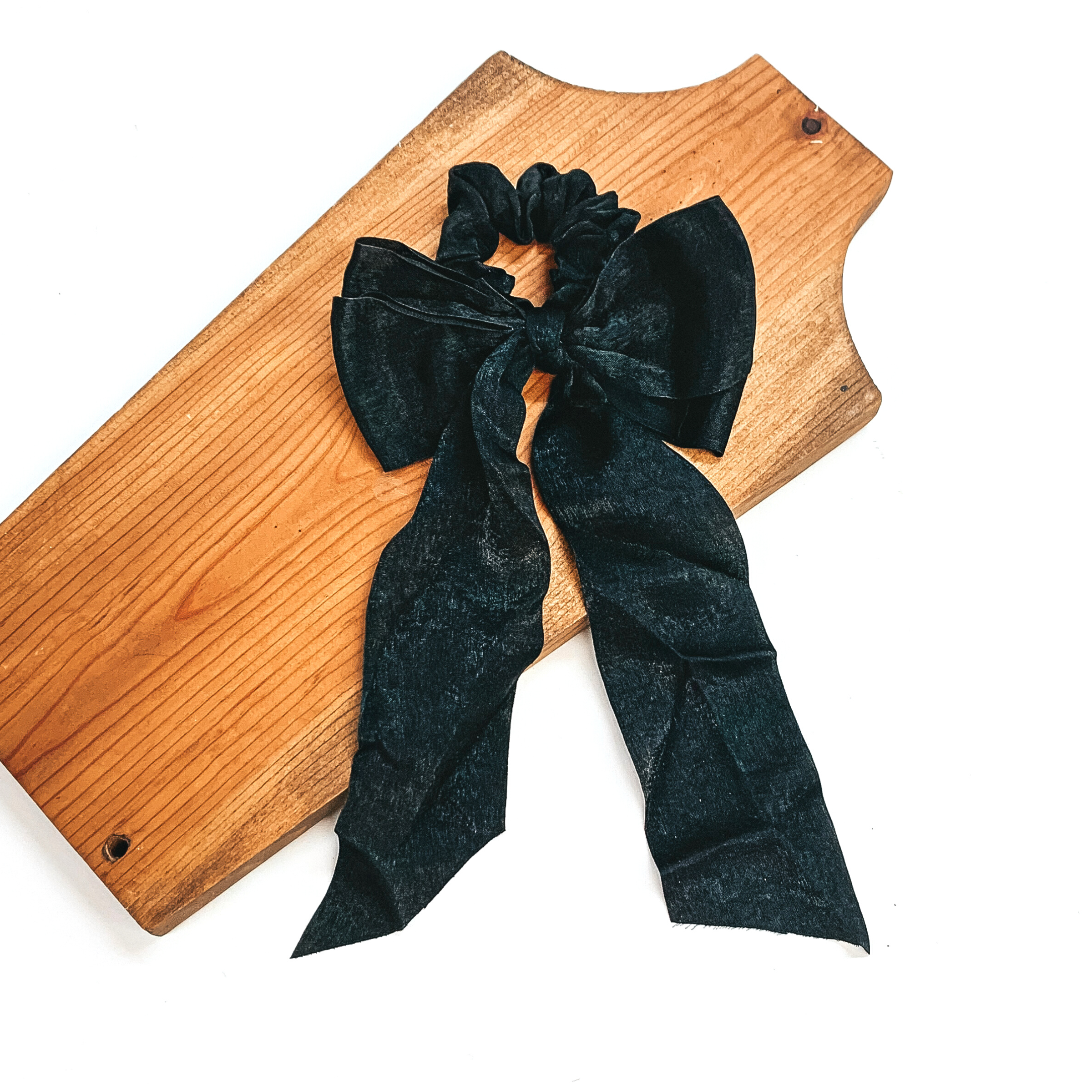 This is a black satin scrunchie with a long bow, this scrunchie is taken on  a brown necklace board and on a white background.