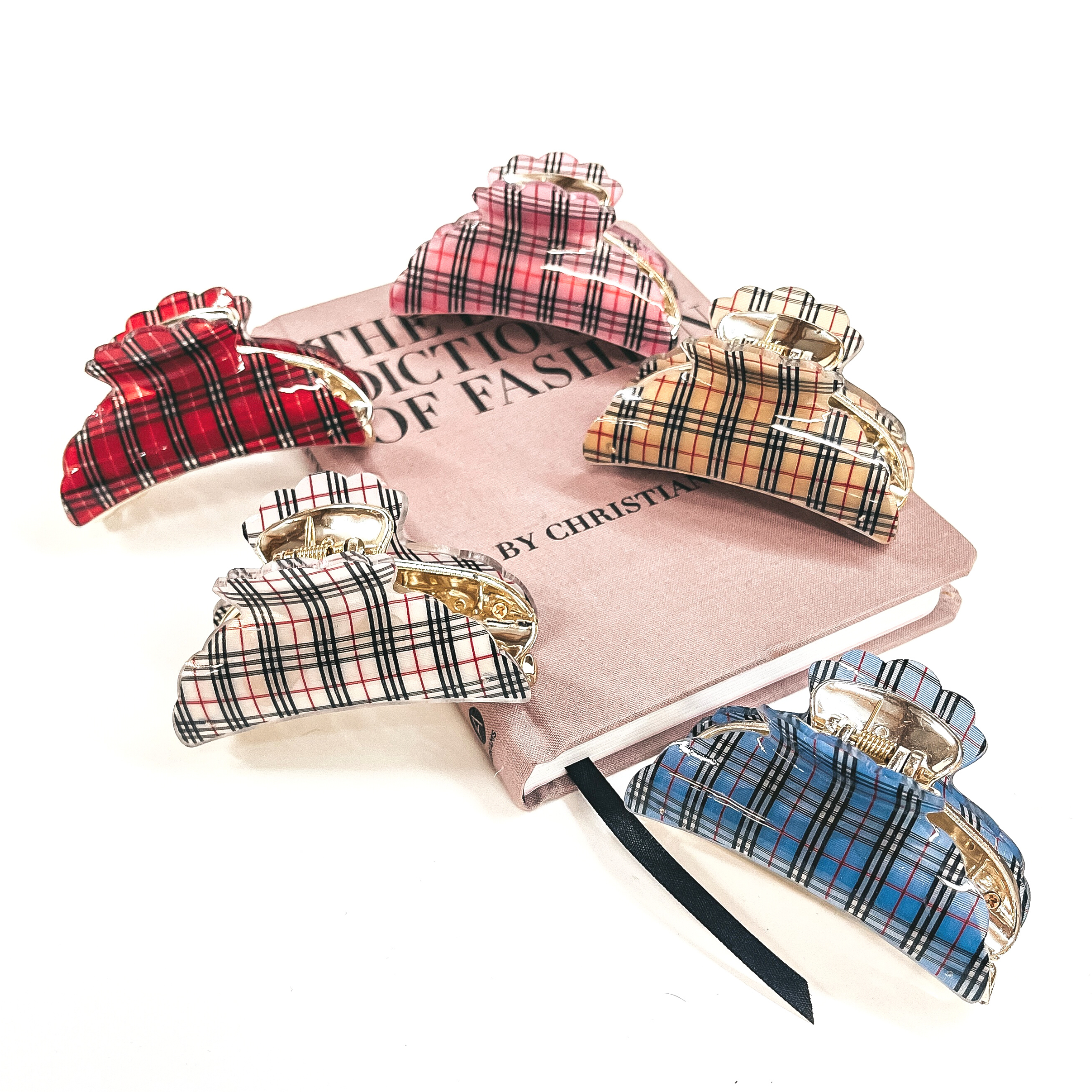 These are five plaid print and gold hair clips laying on a a pink book and on a white background. There is a pink, red, tan, white, and blue plaid print clips.