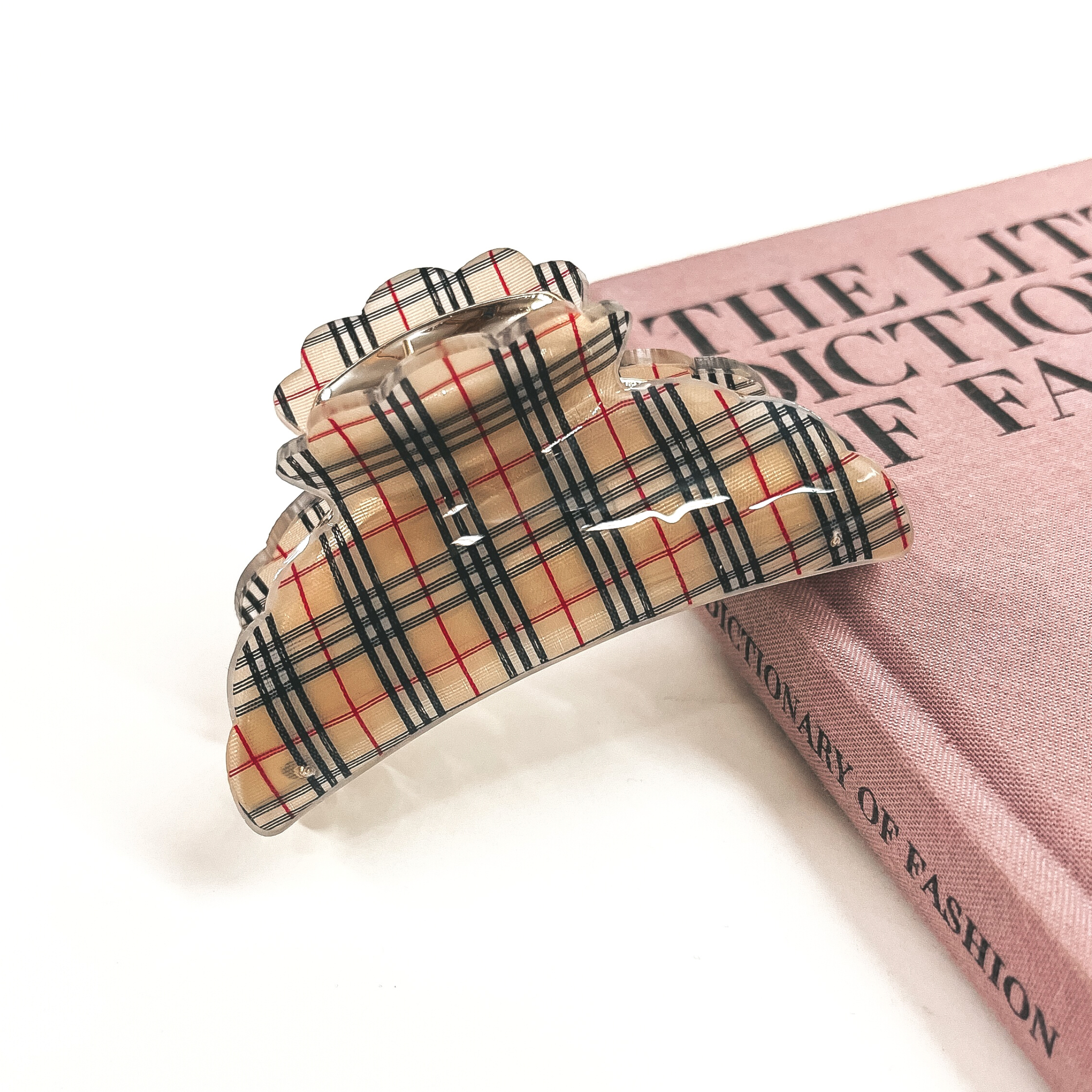 This is a gold and tan plaid print hair clip laying on the side of a pink book and white background.
