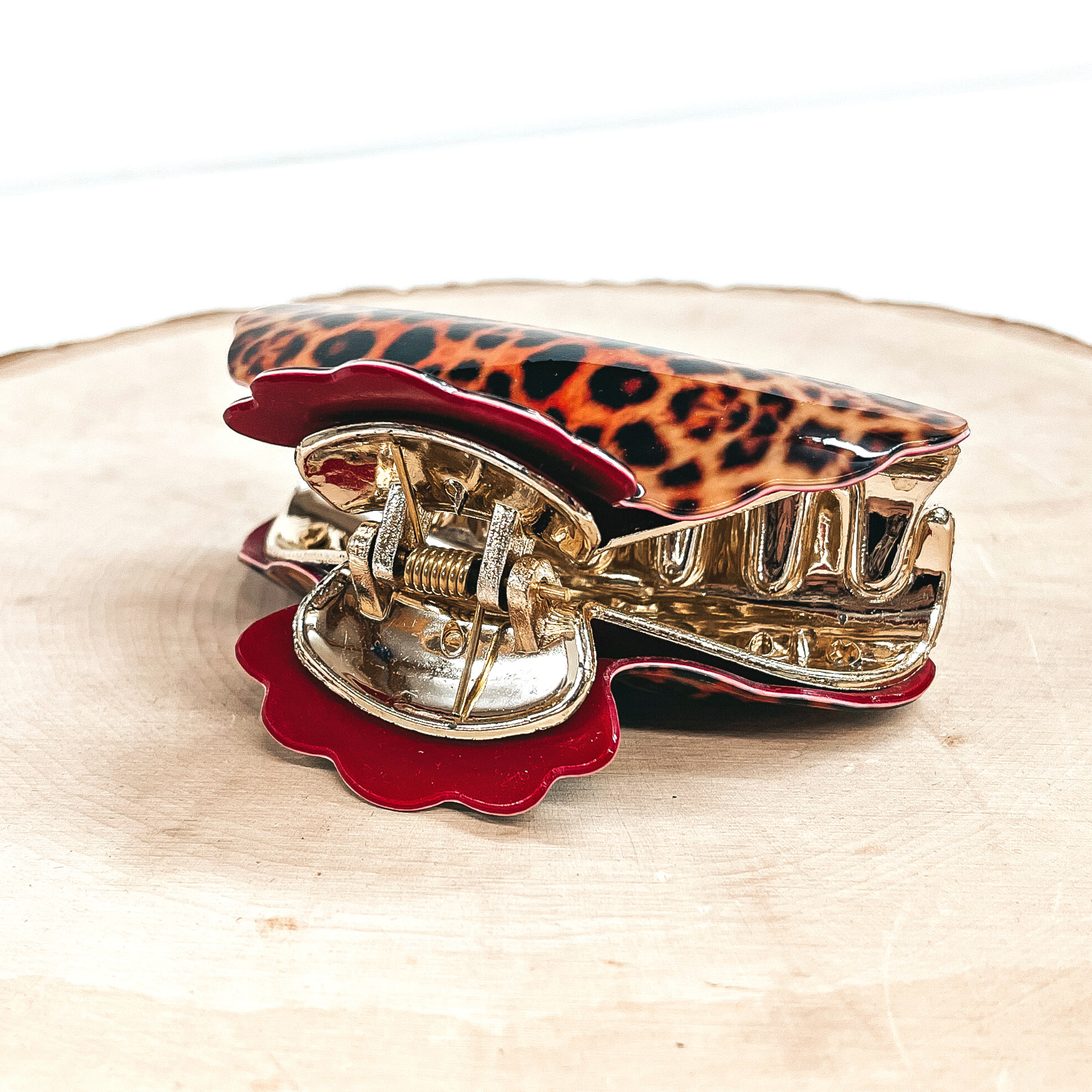This is an orange leopard print hair clip in red in a gold inlay.  This hair clip is taken on a slab of wood and a white  background.