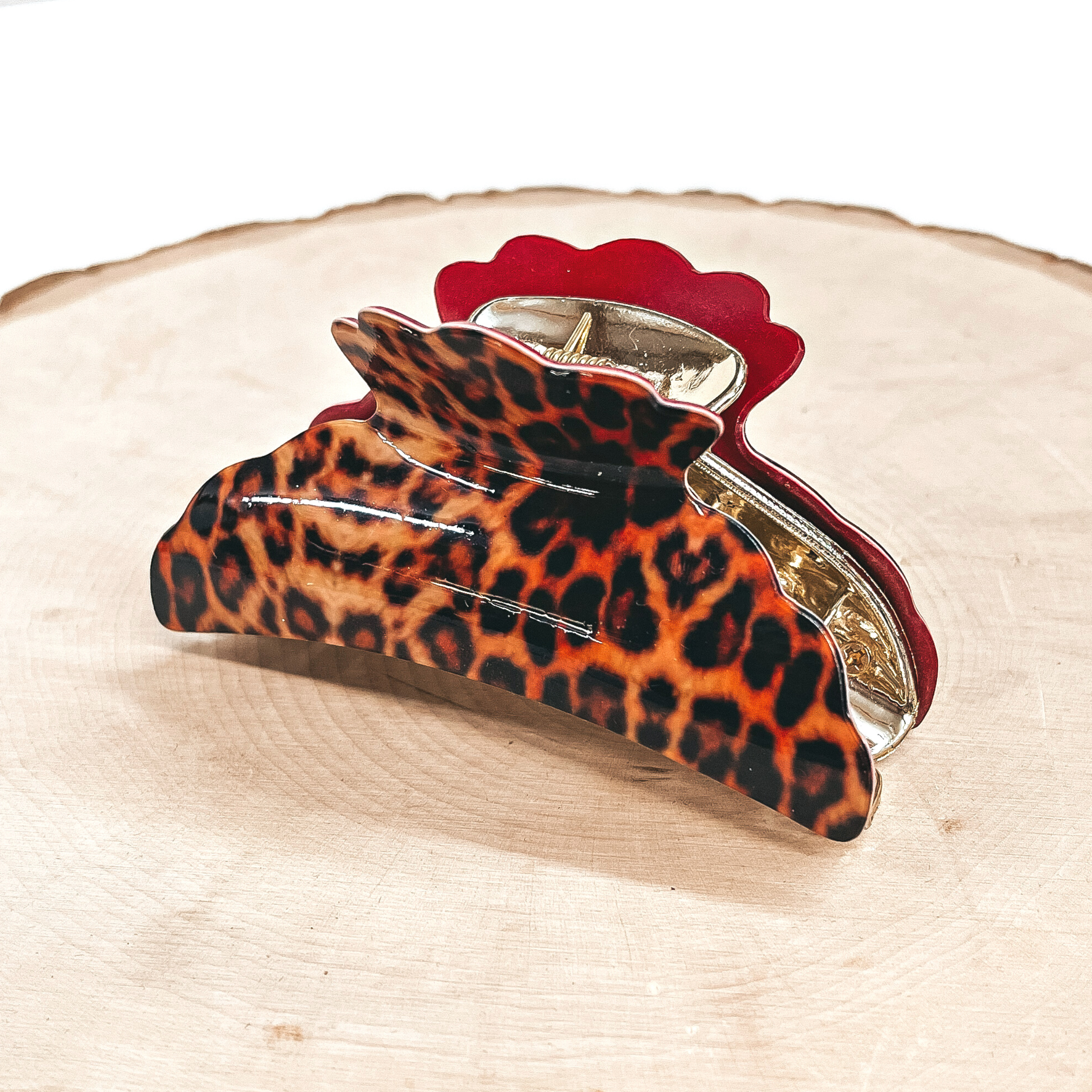 This is an orange leopard print hair clip in red in a gold inlay.  This hair clip is taken on a slab of wood and a white  background.