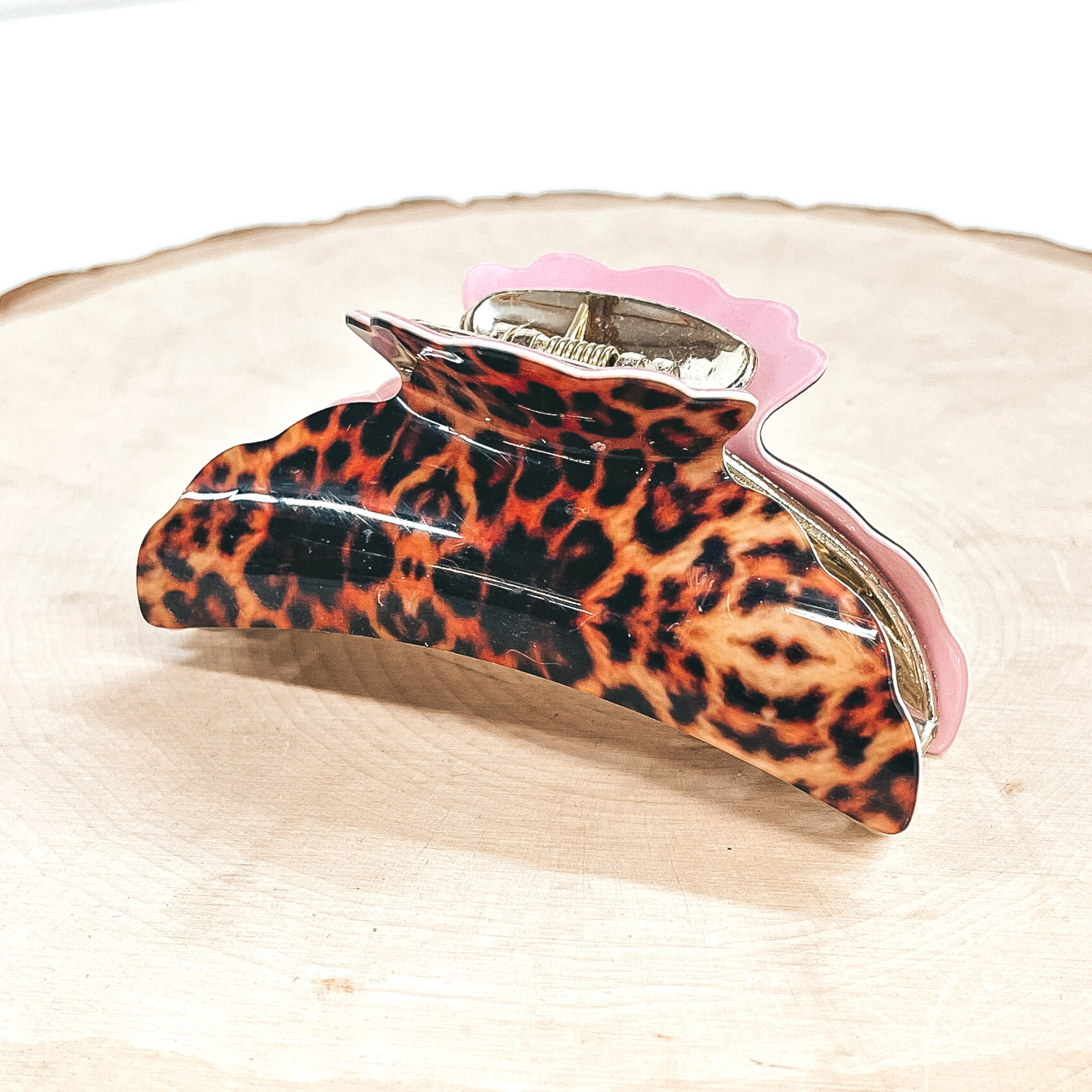This is an orange leopard print hair clip in light pink in a gold inlay.  This hair clip is taken on a slab of wood and a white  background.