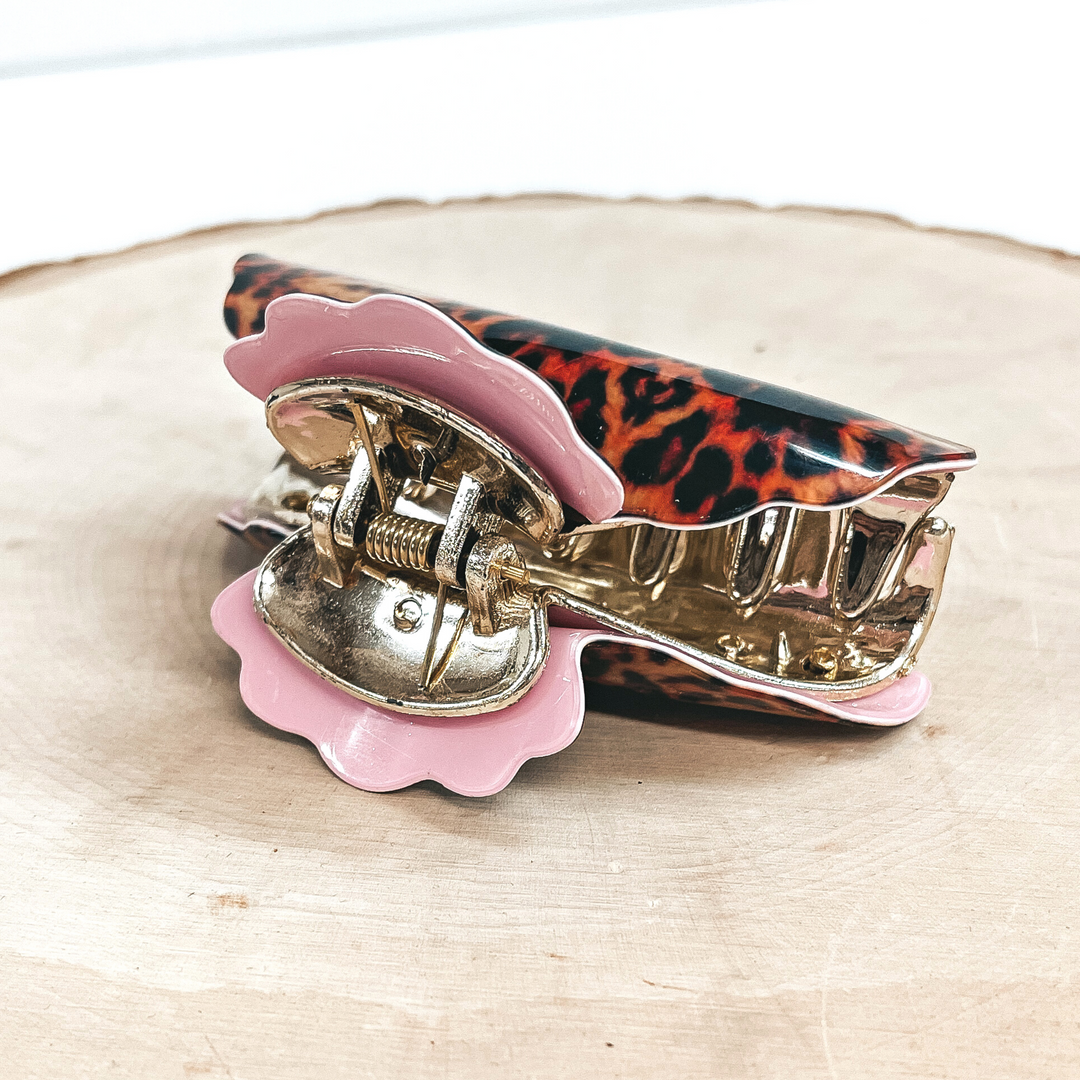 This is an orange leopard print hair clip in light pink in a gold inlay.  This hair clip is taken on a slab of wood and a white  background.