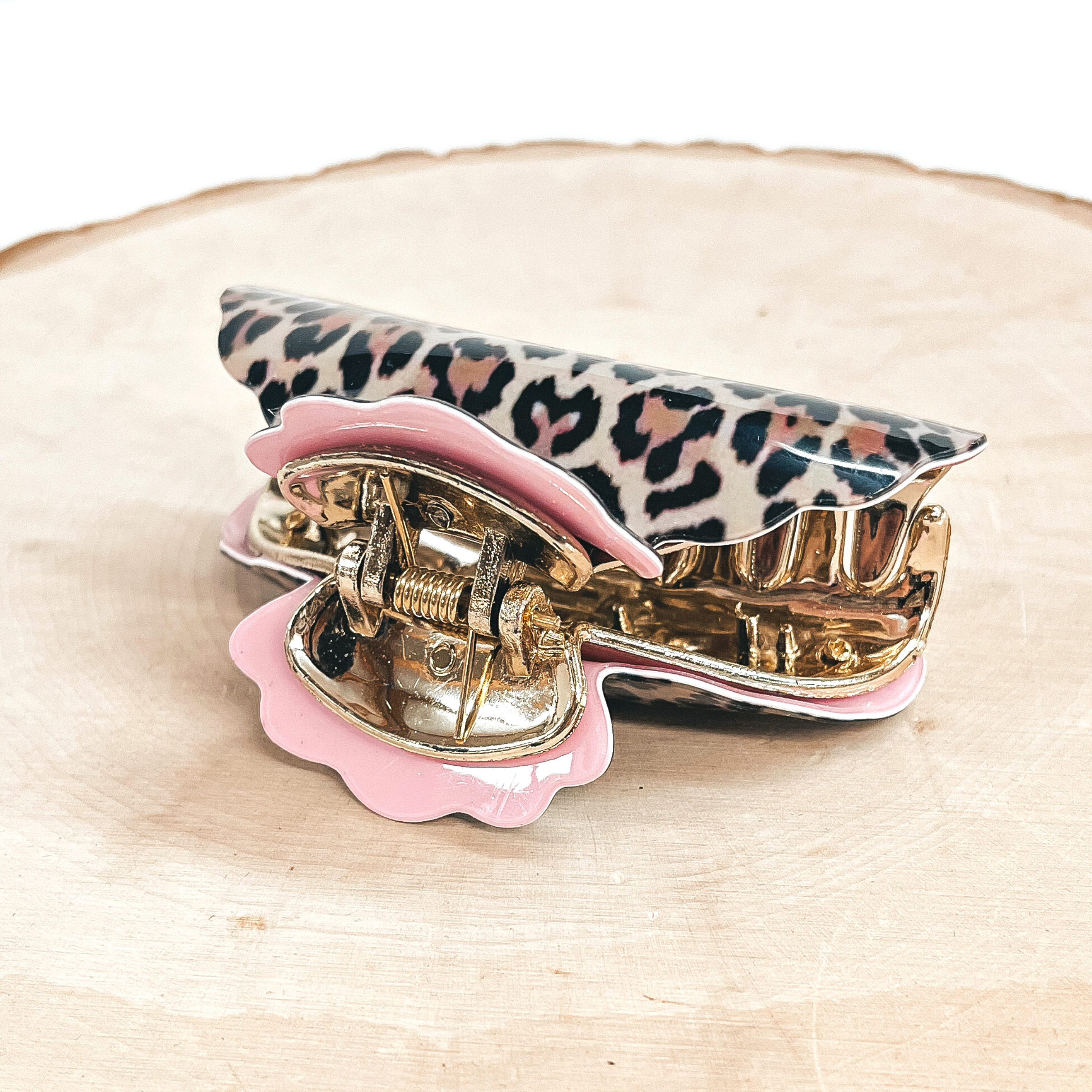 This is a light brown leopard print hair clips in light pink in a gold tone inlay.  This hair clip is  taken on a slab of wood and white background.