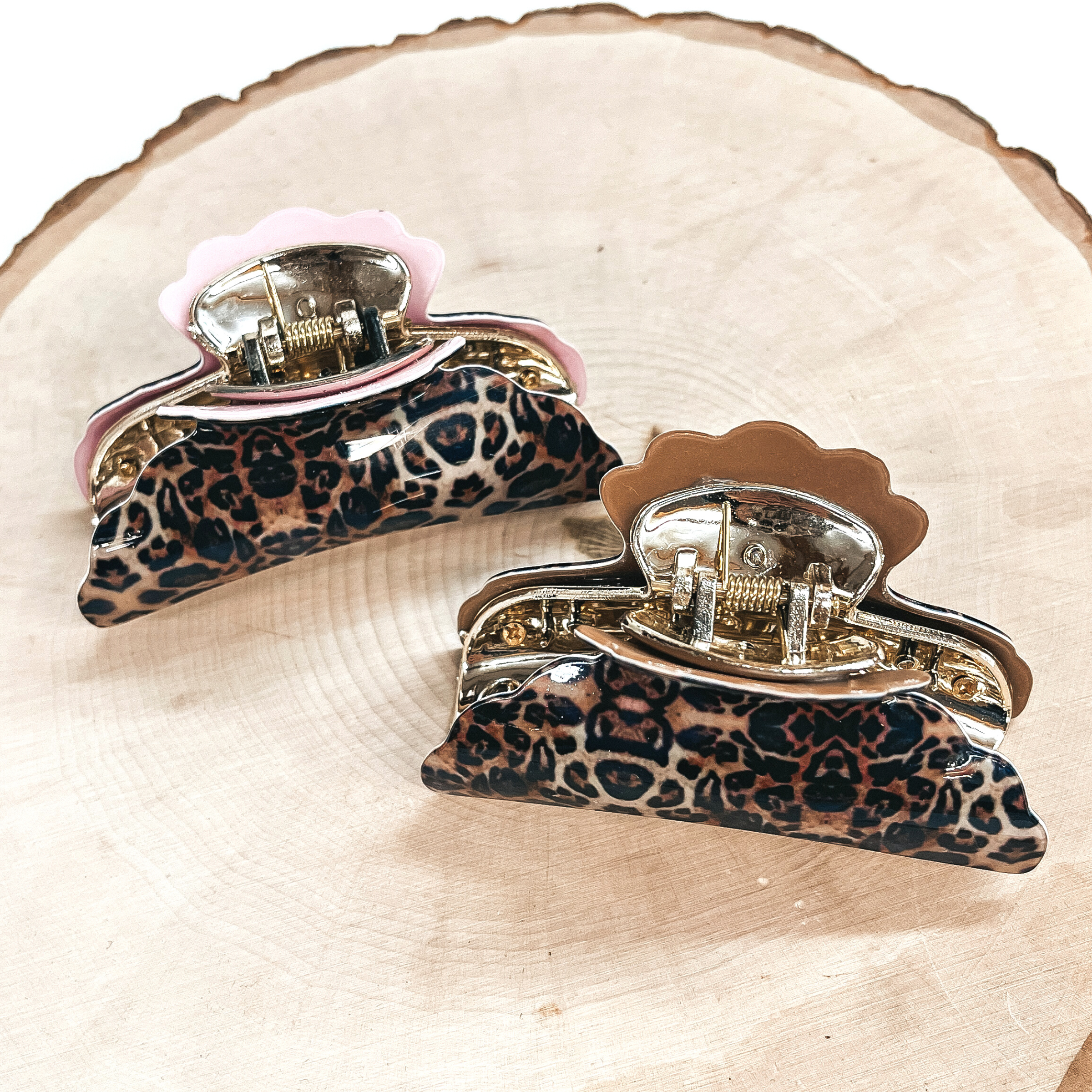 These are small leopard print hair clips with a gold tone inlay in light pink and light  brown.   Both of these hair clip are taken on a slab of wood and on a white background.
