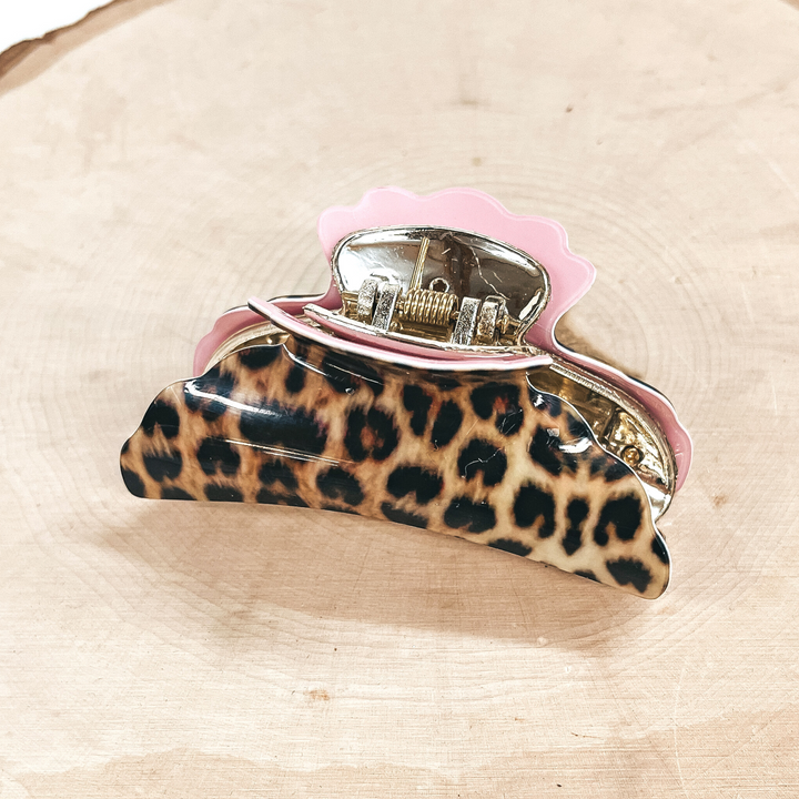 This is a yellow leopard print hair clip with a gold tone inlay in light pink.   This hair clip is taken on a slab of wood and on a white background.