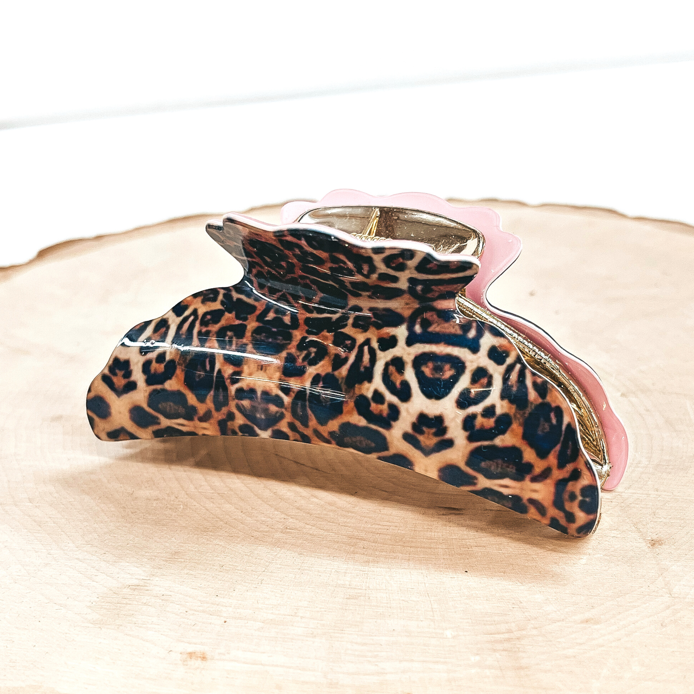 This is a small leopard print hair clips with a gold tone inlay in light pink.   This hair clip is taken on a slab of wood and on a white background.