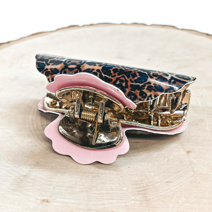 This is a small leopard print hair clips with a gold tone inlay in light pink.   This hair clip is taken on a slab of wood and on a white background.