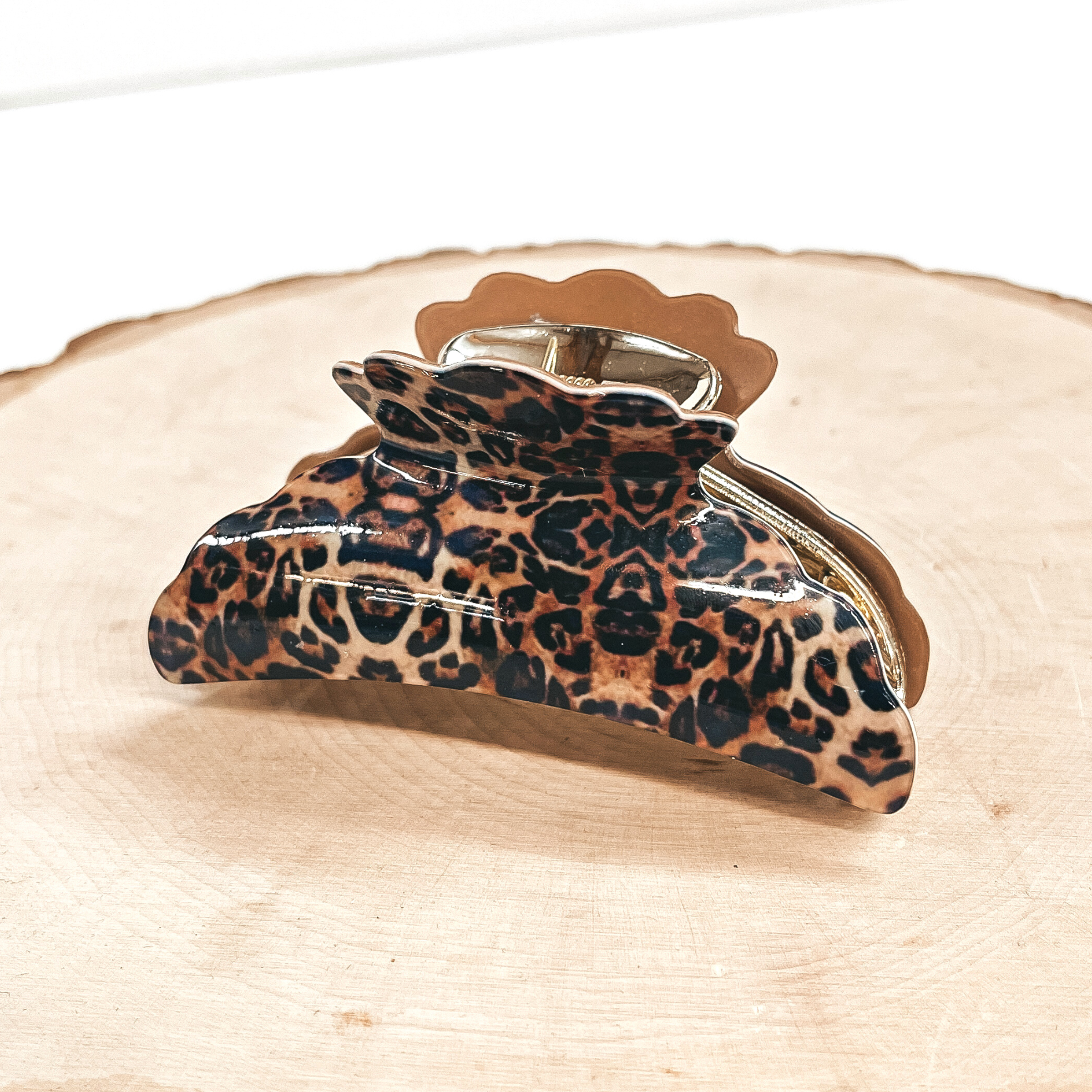 This is a small leopard print hair clips with a gold tone inlay in light brown.   This hair clip is taken on a slab of wood and on a white background.