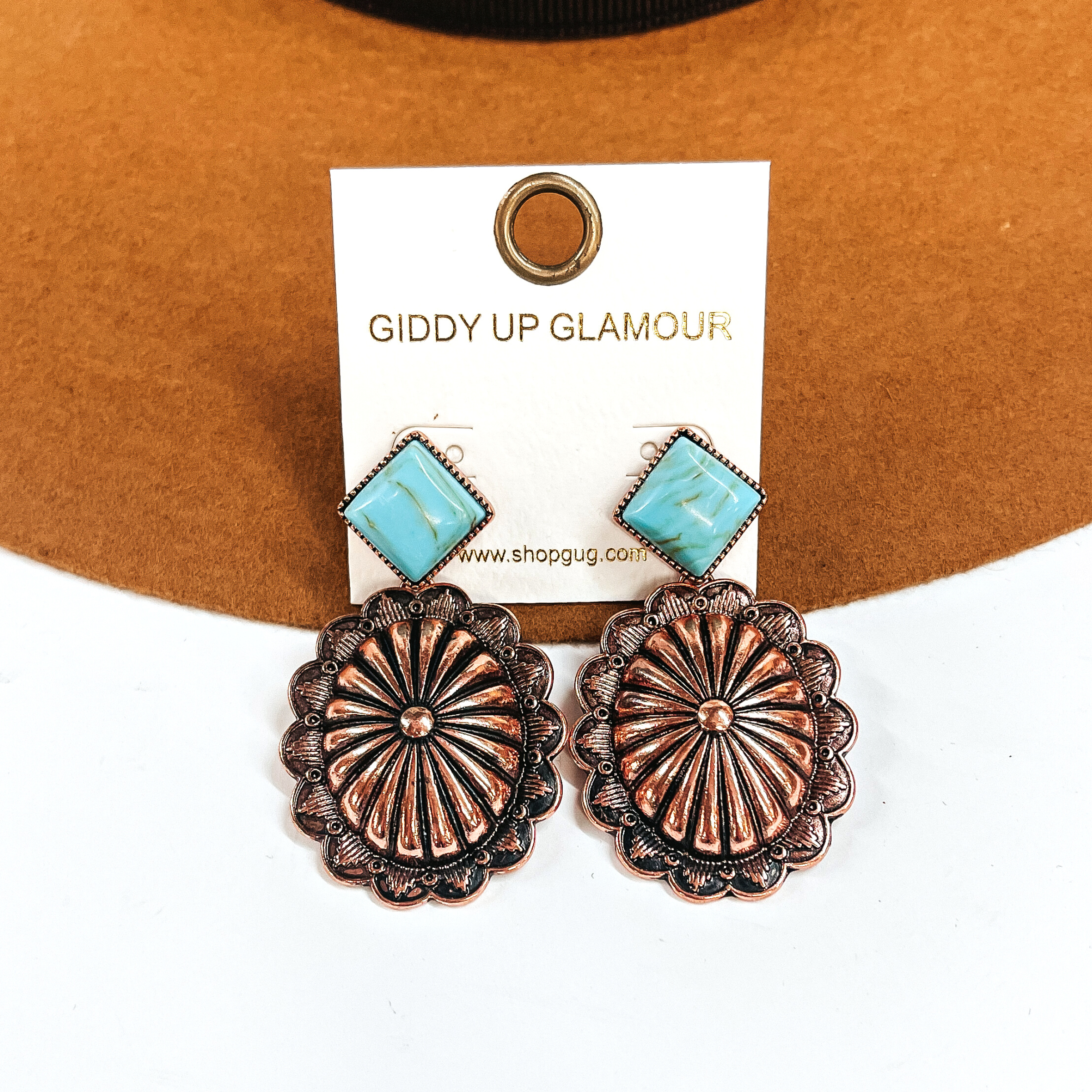 These are copper concho drop earrings with a turquoise-marble stone post in a copper  setting. These earrings are taken laying on a camel felt hat and on a white background.