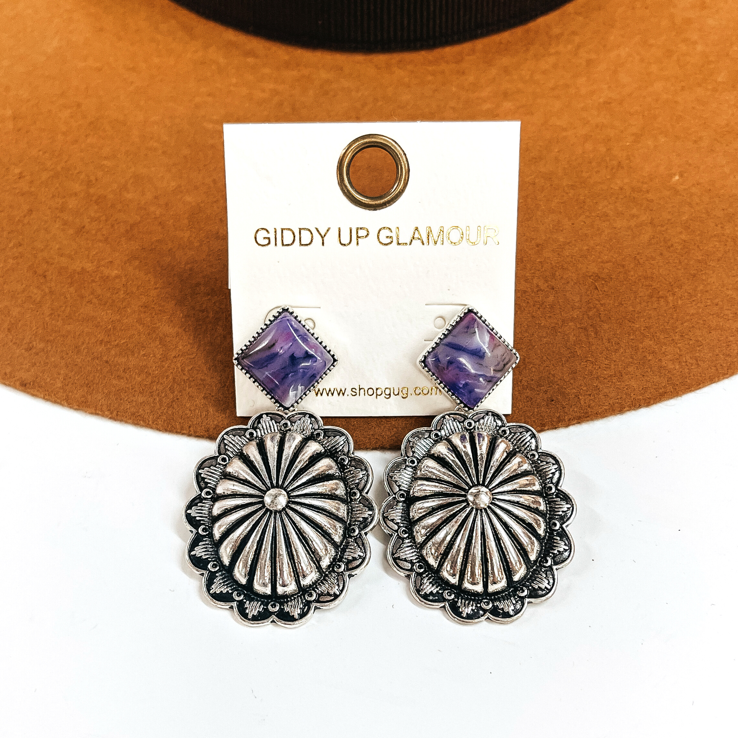 These are silver concho drop earrings with a purple-marble stone post in a silver  setting. These earrings are taken laying on a camel felt hat and on a white background.