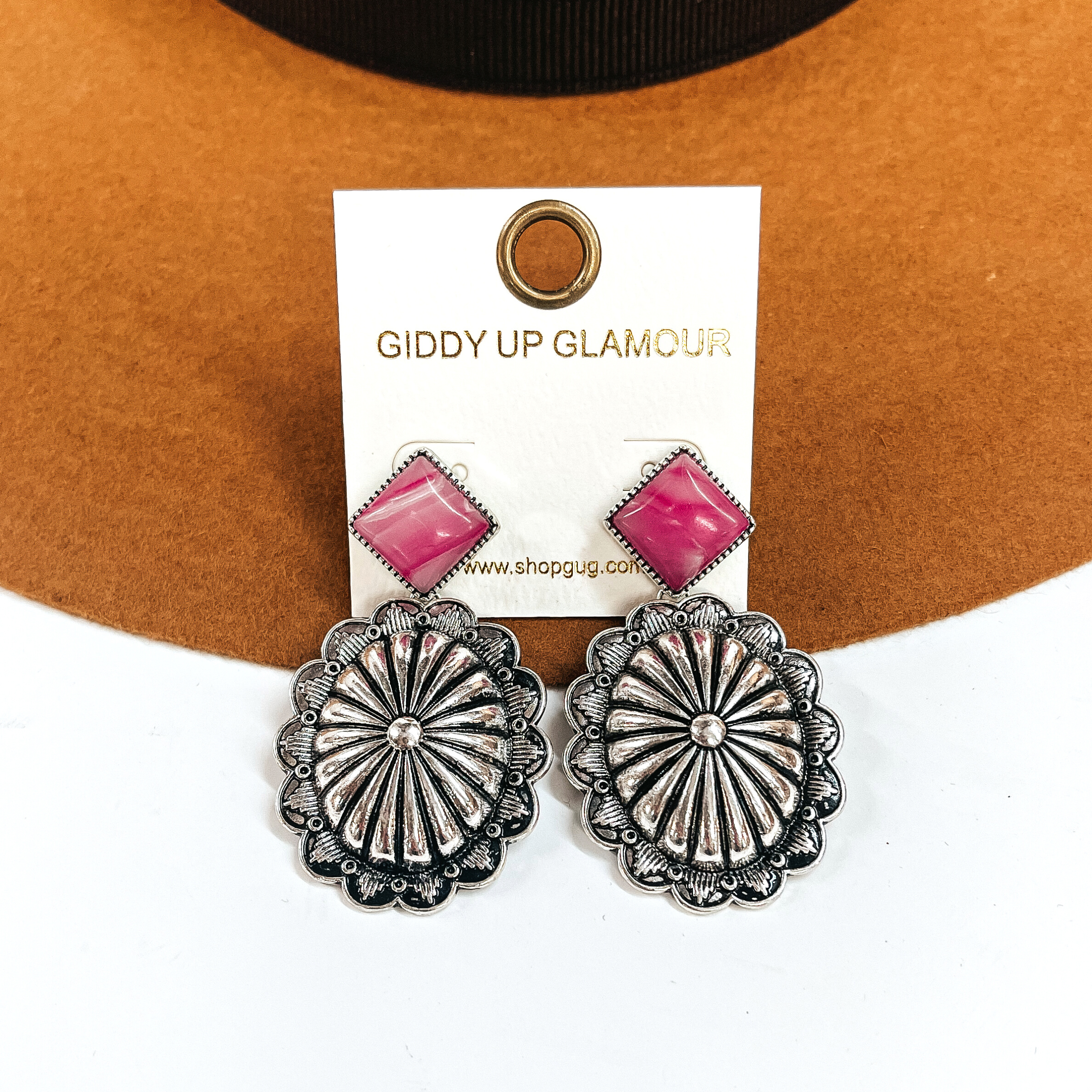 These are silver concho drop earrings with a pink-marble stone post in a silver  setting. These earrings are taken laying on a camel felt hat and on a white background.