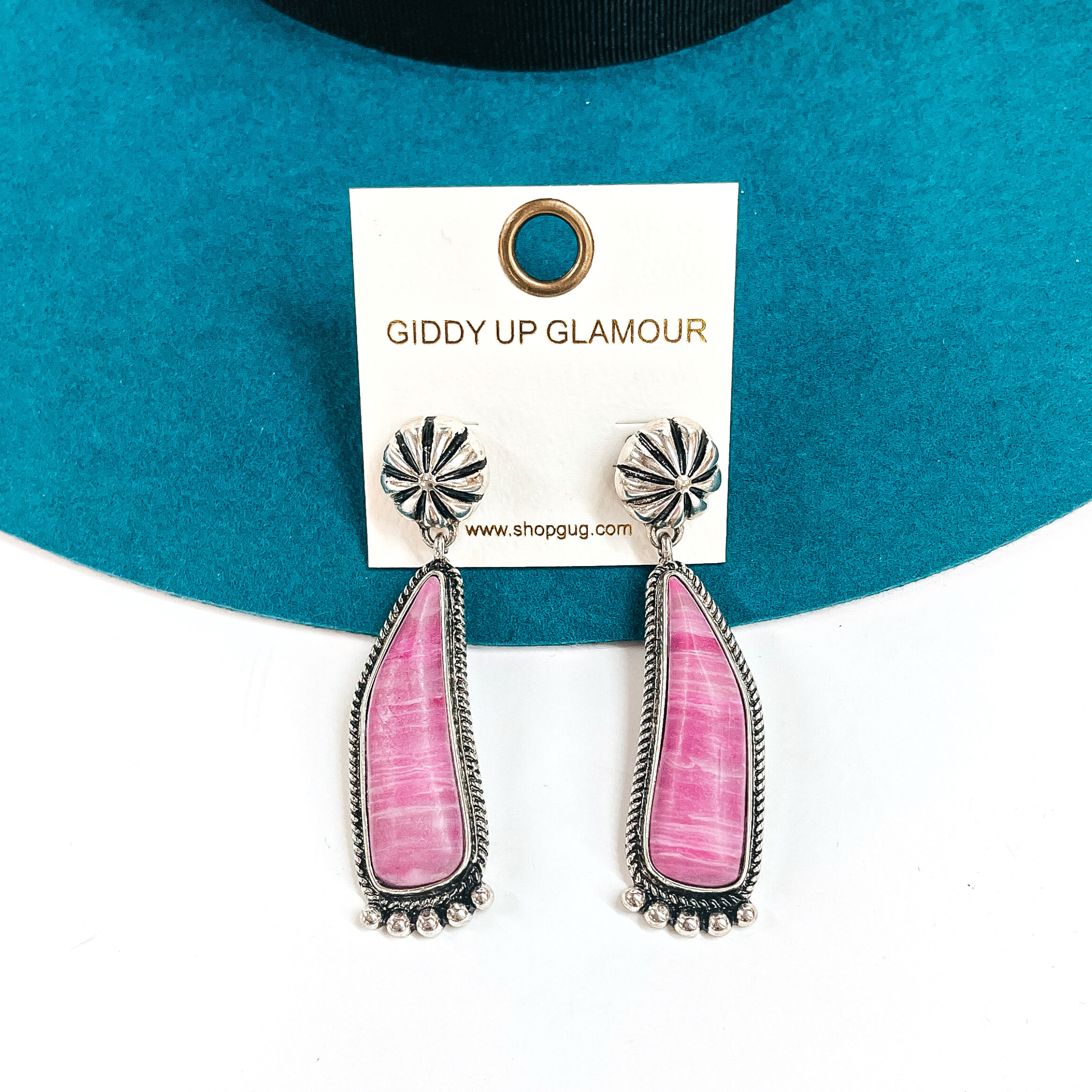 These are silver conch post earrings with a pink-marble stone drop earrings in a  silver setting. They have silver details in the bottom and they ae slightly curved.  These earrings are taken laying on a teal felt hat and on a white background.