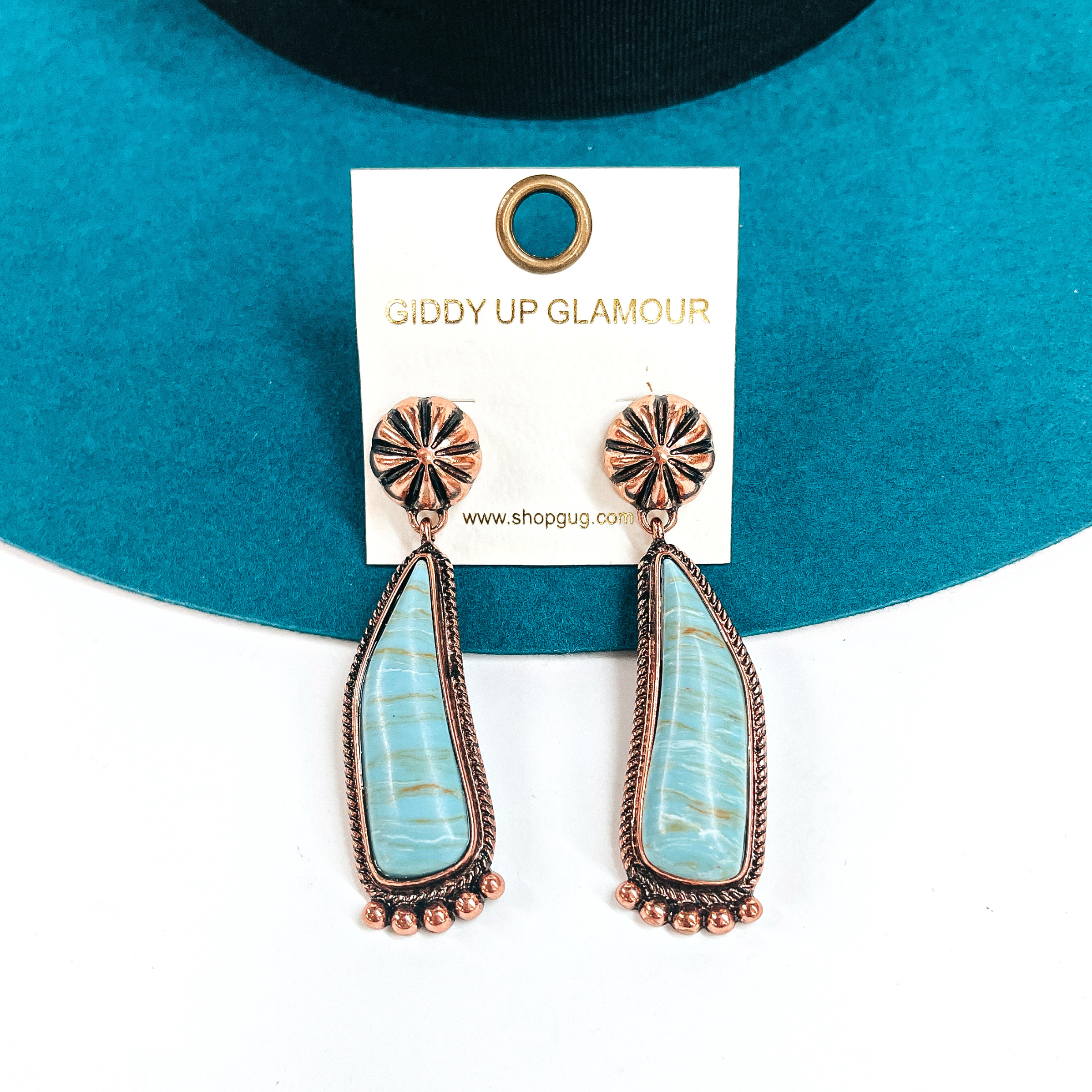 These are copper conch post earrings with a turquoise-marble stone drop earrings in a  copper setting. They have copper details in the bottom and they ae slightly curved.  These earrings are taken laying on a teal felt hat and on a white background.