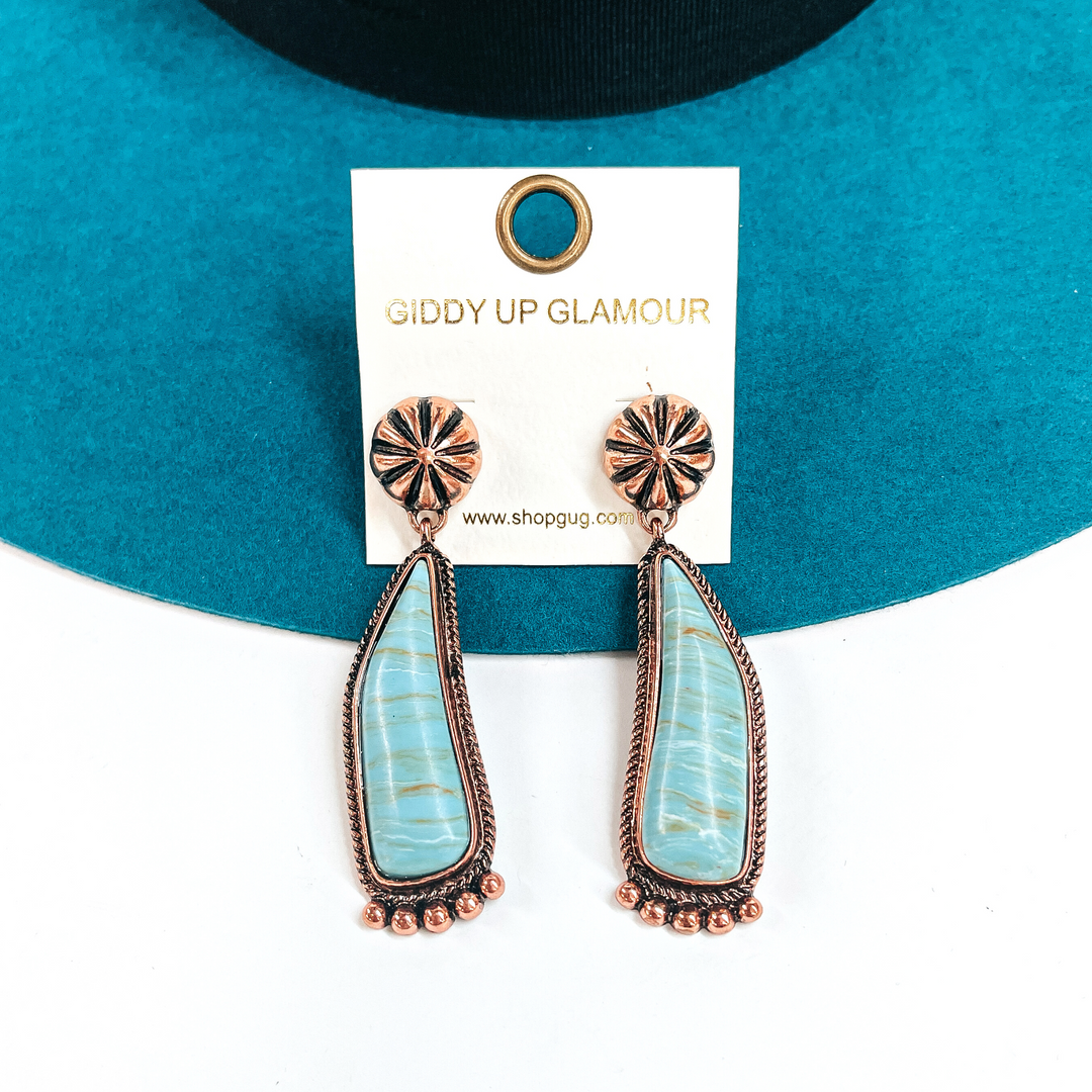 These are copper conch post earrings with a turquoise-marble stone drop earrings in a  copper setting. They have copper details in the bottom and they ae slightly curved.  These earrings are taken laying on a teal felt hat and on a white background.