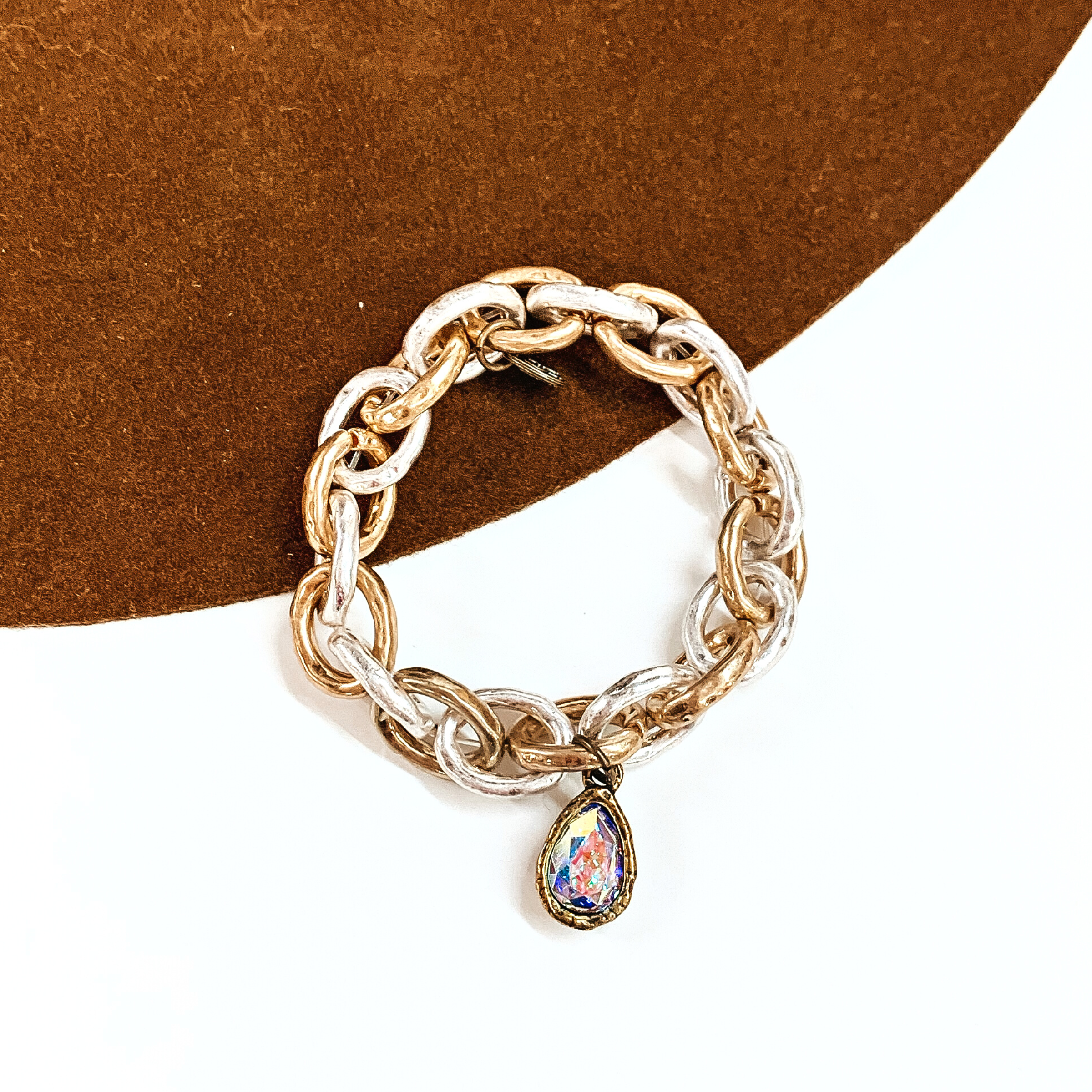 This is gold and silver thick chain bracelets with an AB crystal teardrop charm in a  bronze setting. This bracelet is laying on a brown felt hat and on a white background.