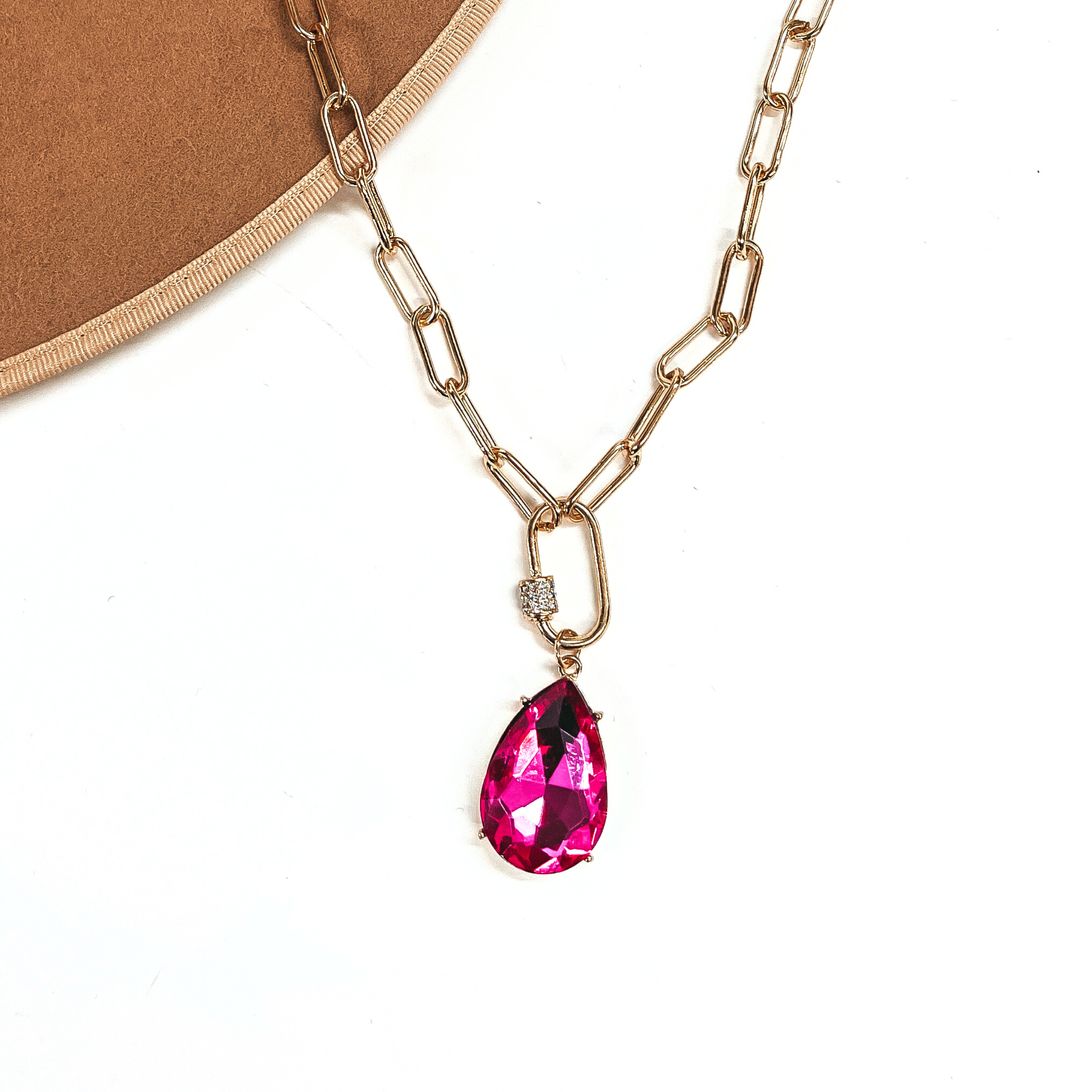 This is a large gold tone link chain necklace with a link connector and a large  fuchsia crystal teardrop. The link connector has a small band of small clear  crystals. This necklace is taken laying on a brown felt hat brim and on a white  background.