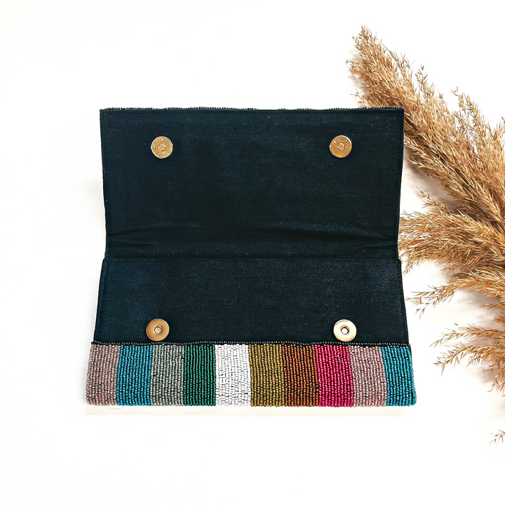 This is the inside of the seedbeaded clutch purse in multicolor line with a black  inside. This bag  is taken laying on a white background with a brown plant in the side as decor.