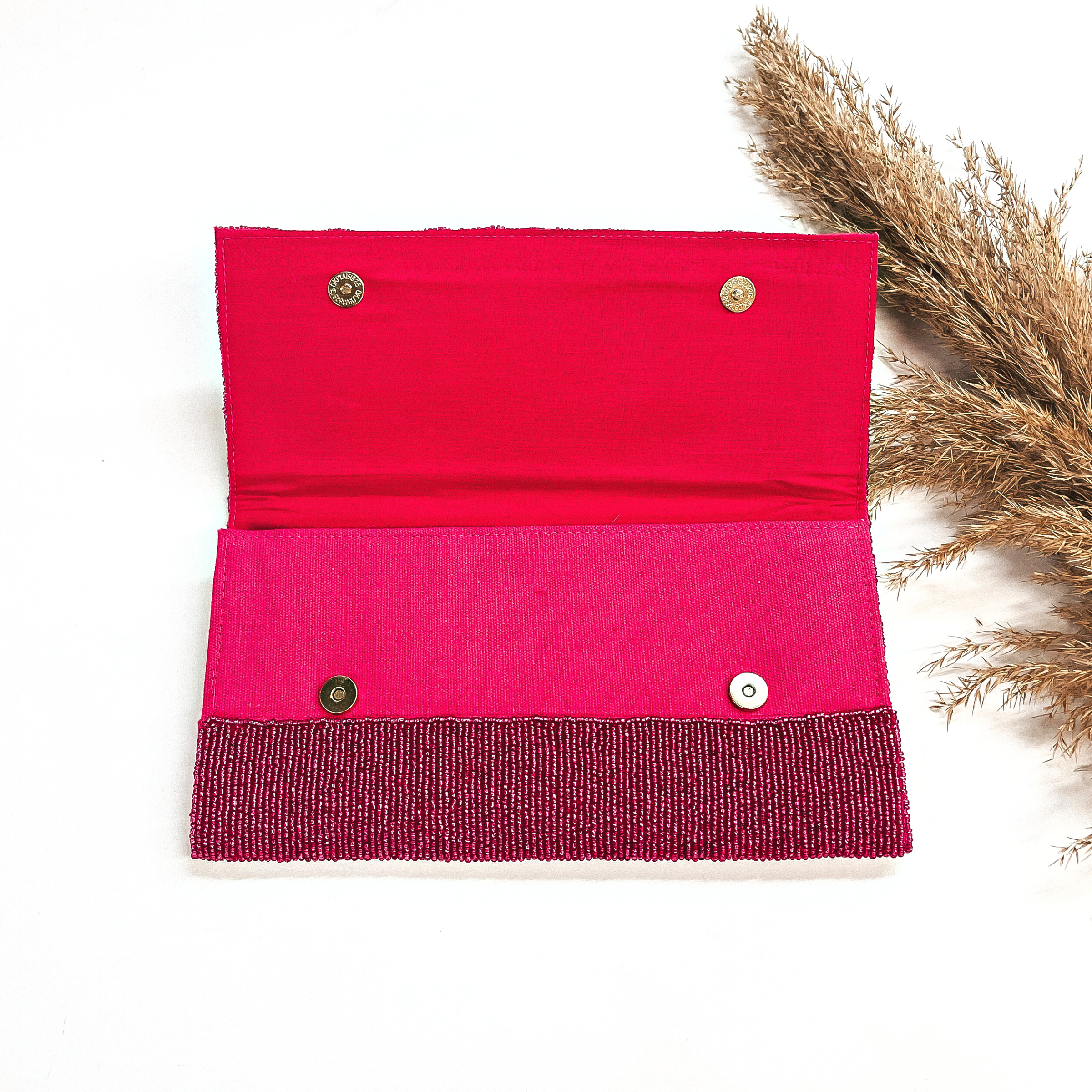 This is the inside of the seedbeaded clutch purse in fuchsia with a pink  inside. This bag  is taken laying on a white background with a brown plant in the side as decor.