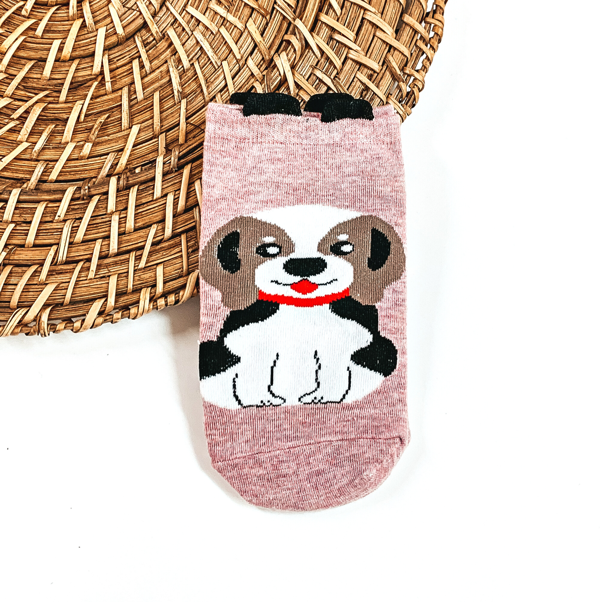 This is a light pink pair of socks with a brown/white Beagle and red collar. There  are small black ears on top on the socks.  This pair of socks are taken on a brown woven slate and on a white  background.
