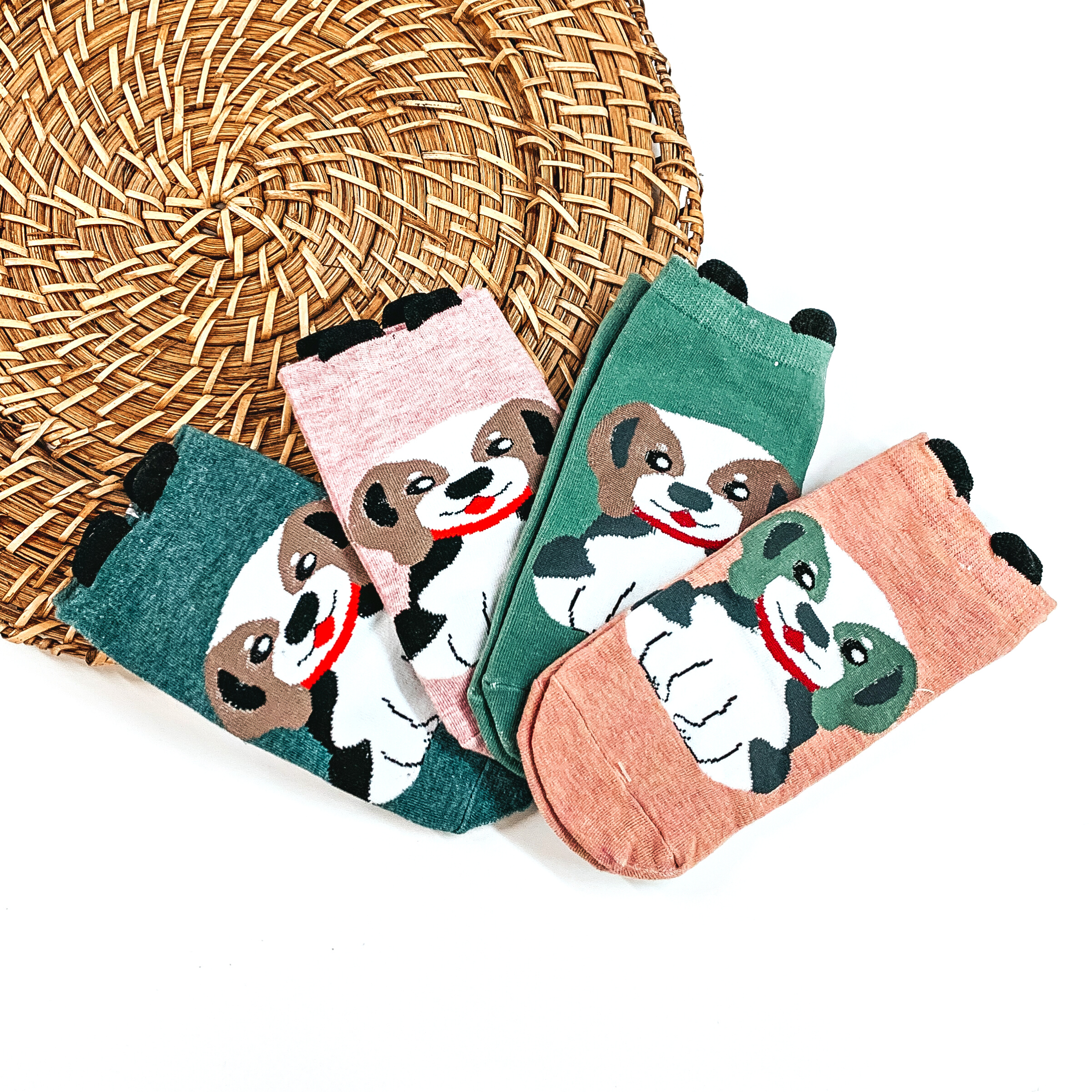 There are four pairs of socks with a Beagle dog on the center and they have small  black 'ears' on the top. From left to right; dark green with a brown/white Beagle  and a red collar, light pink with a brown/white Beagle and a red collar, green with  a brown/white Beagle and a red collar, and then coral with a green/white Beagle with  a red collar. These pair of socks are taken on a brown woven slate and on a white  background.