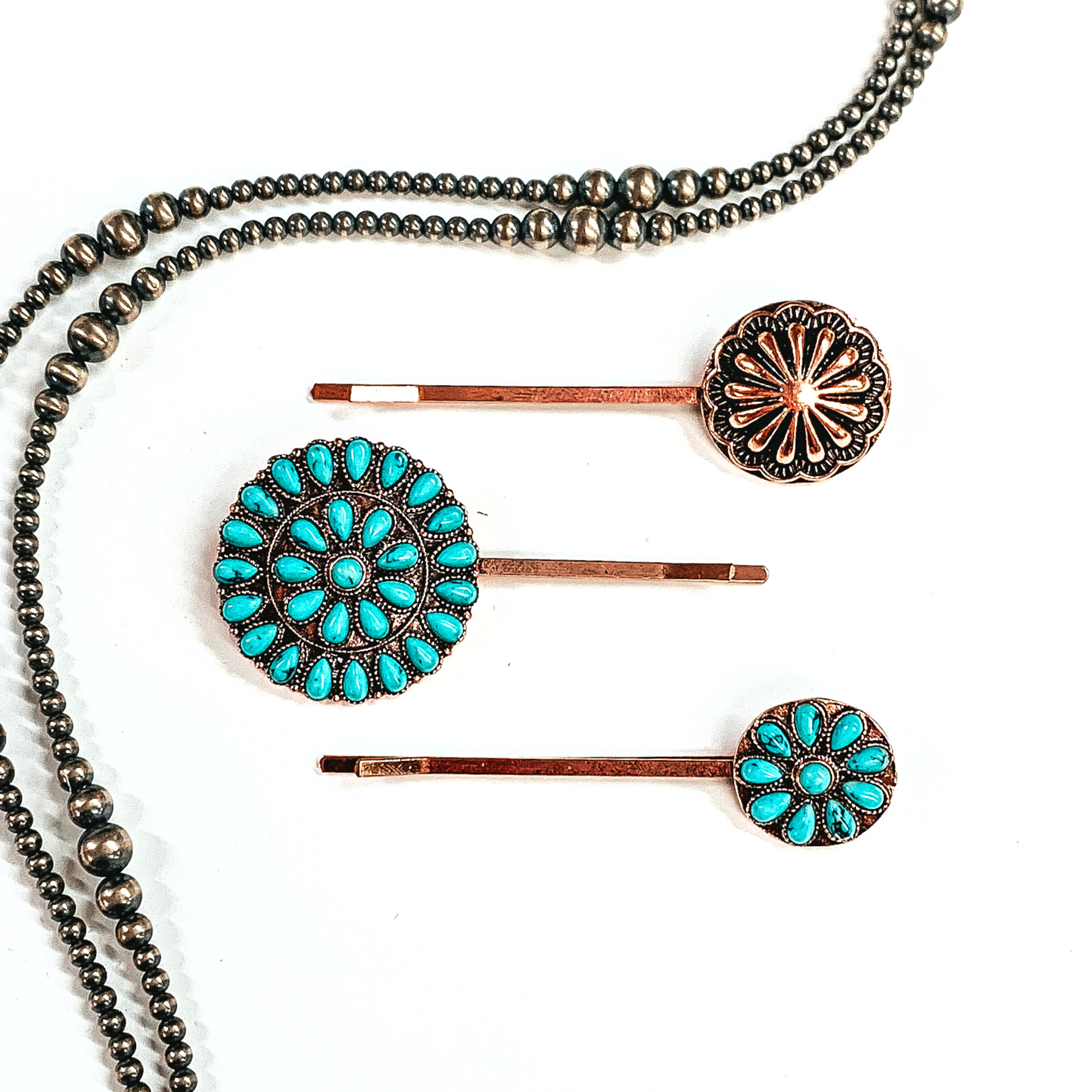 There are three copper bobby pins with conchos and faux turquoise clusters. From  top to bottom; copper concho, large circle stone cluster, small circle stone cluster. These bobby pins are taken on a white background  with silver navajo pearls around as decor.