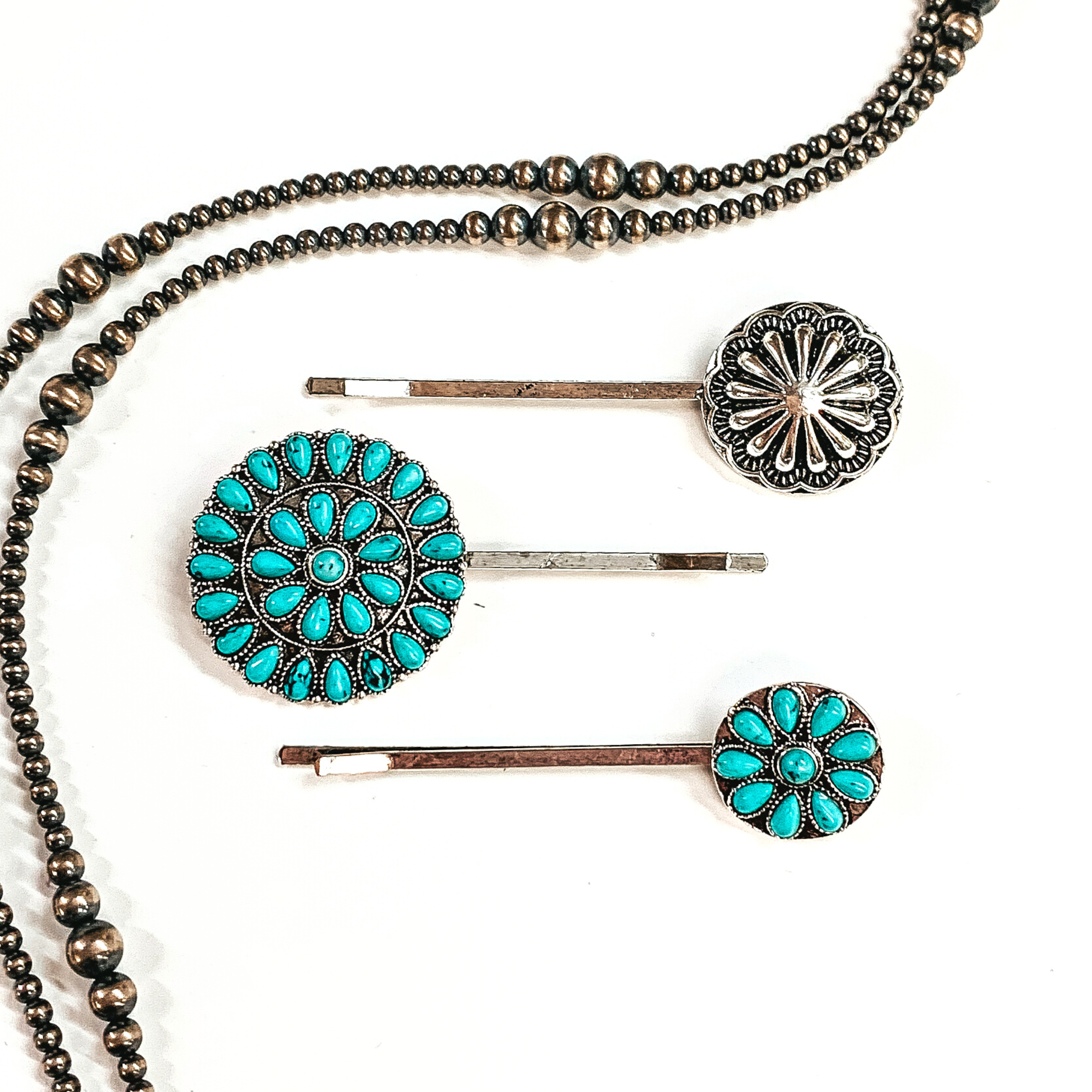 There are three silver bobby pins with conchos and faux turquoise clusters. From  top to bottom; silver concho, large circle stone cluster, small circle stone cluster. These bobby pins are taken on a white background  with silver navajo pearls around as decor.