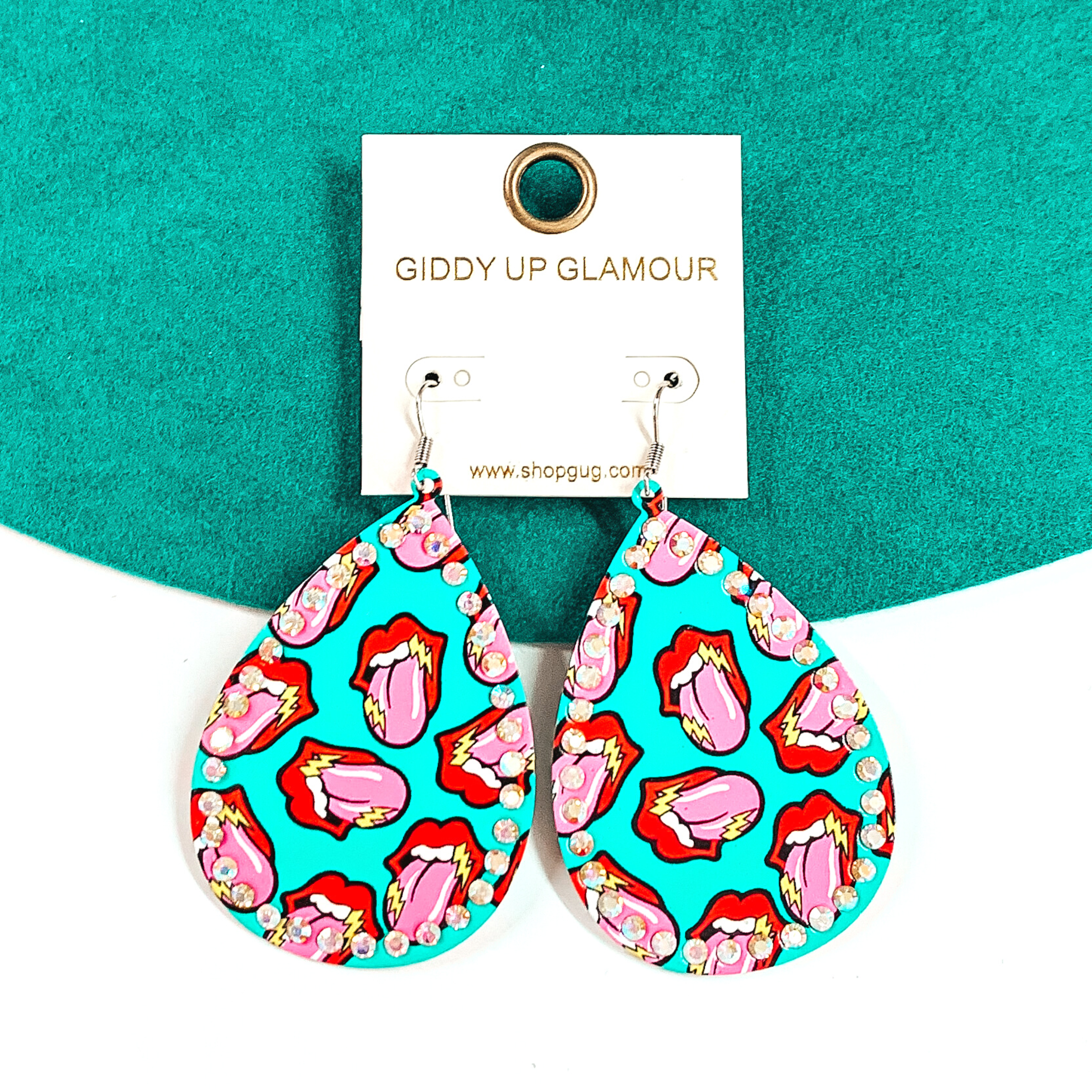 These are turquoise, teardrop, lip and tongue print earrings with ab crystal all around.  The lip is red with a pink tongue and yellow lightning bolts on each tongue and lip. These earrings are taken on a green-teal felt hat brim and on a white background.