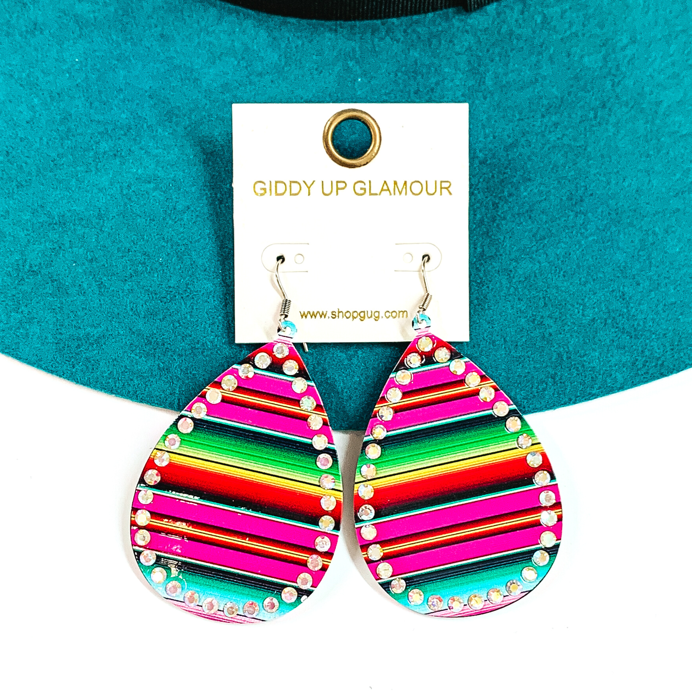 These are teardrop serape print earrings with ab crystals all around. The serape print  is in a pink mix such as; pink, blue, turquoise, green, and a bit of red. These  earrings are taken on a teal felt hat brim and on a white background.