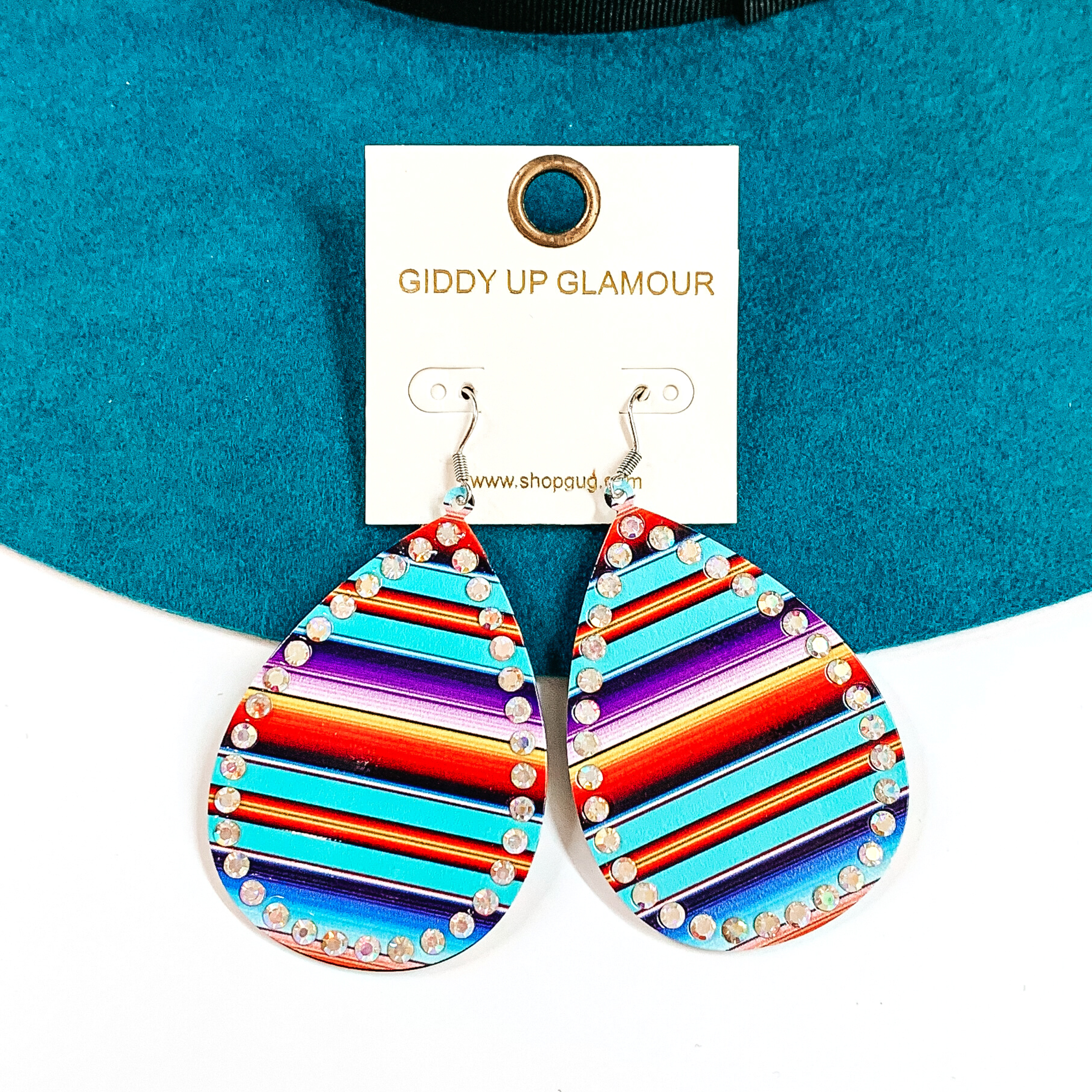 These are teardrop serape print earrings with ab crystals all around. The serape print  is in a turquoise mix such as; turquoise, purple, orange, blue, and a bit of yellow.  These  earrings are taken on a teal felt hat brim and on a white background.