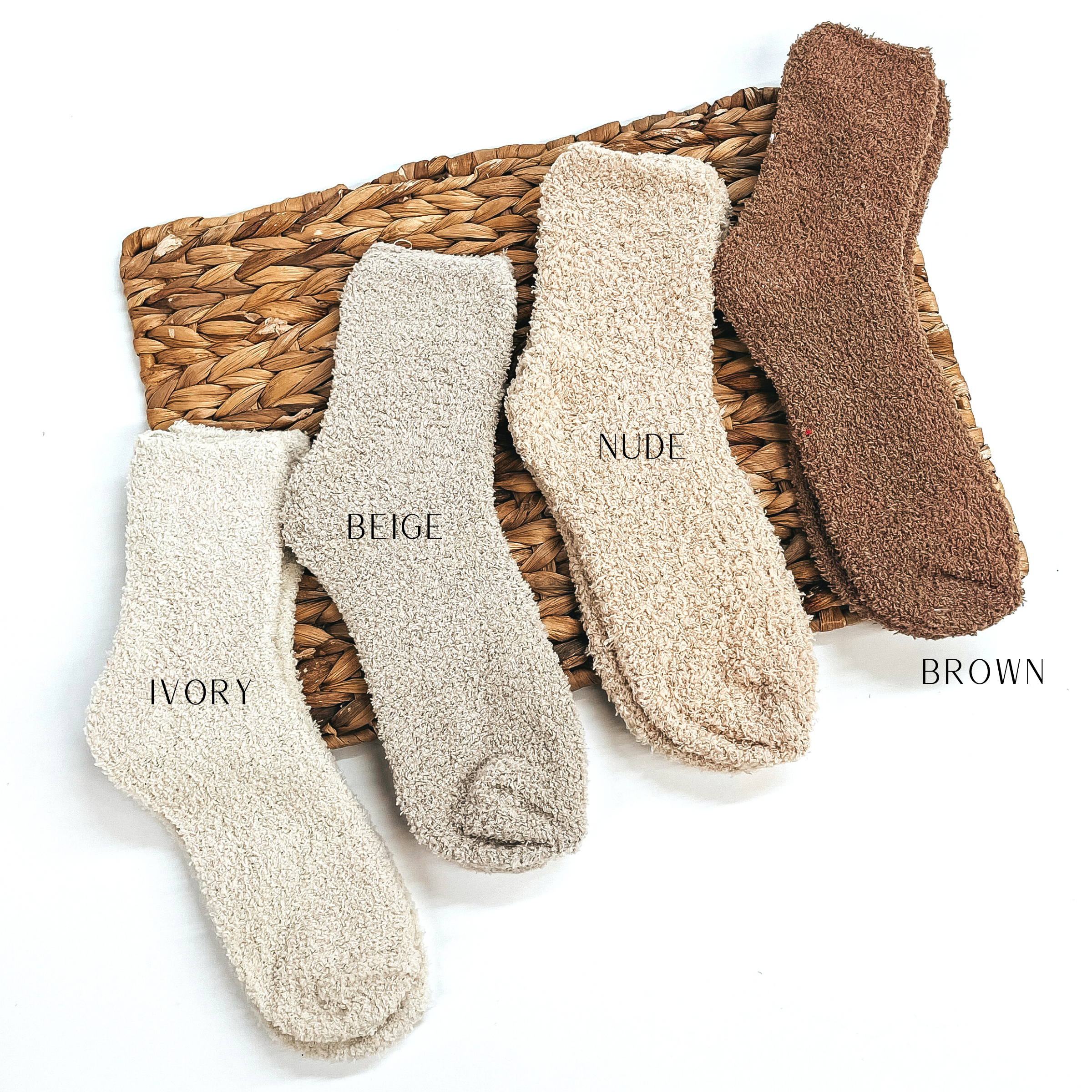 These are four pairs of fuzzy socks, from left to right; ivory, beige, nude,  and brown. These socks are taken on a brown woven slate and on a white  background.