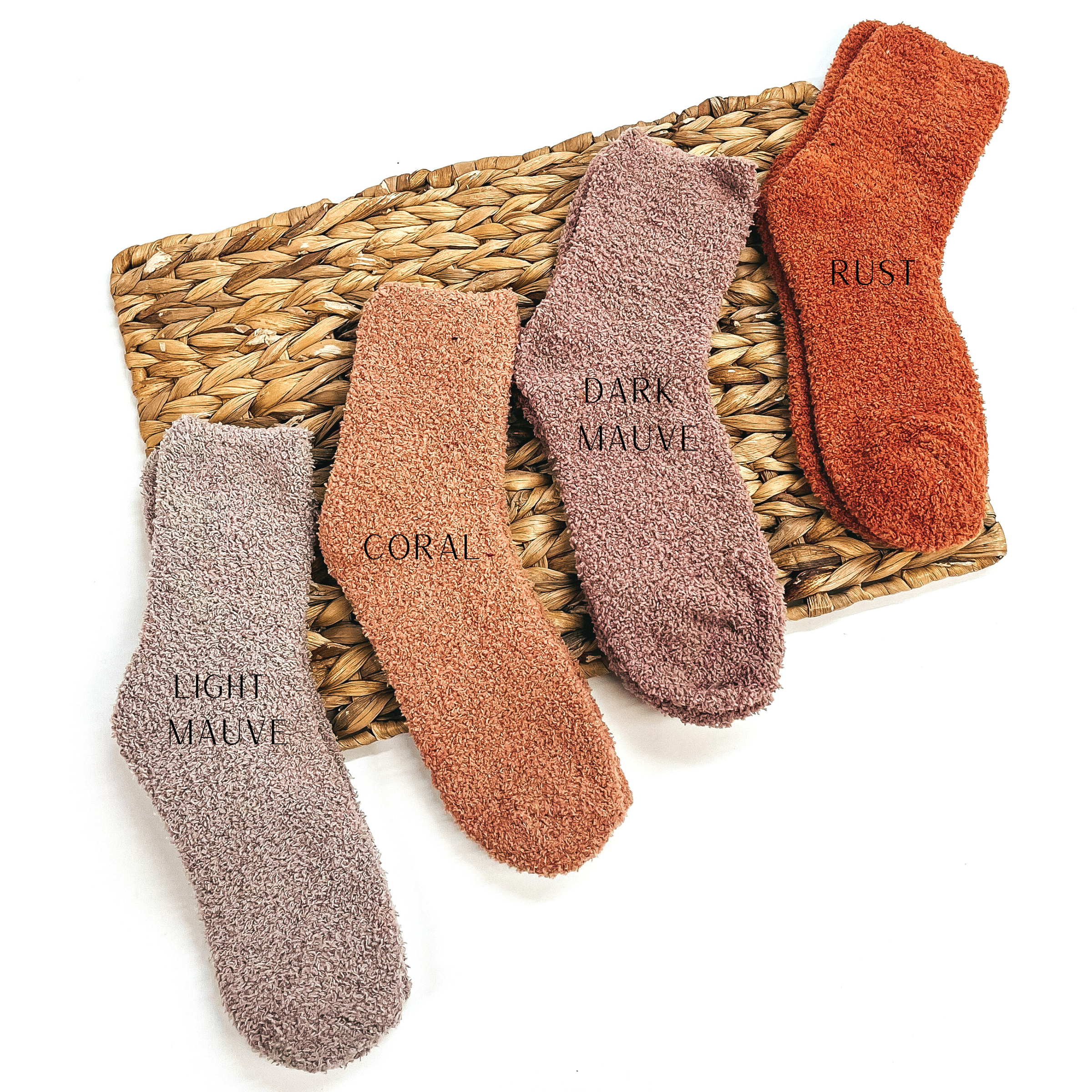 These are four pairs of fuzzy socks, from left to right; light mauve, coral, dark mauve,  and rust. These socks are taken on a brown woven slate and on a white  background.