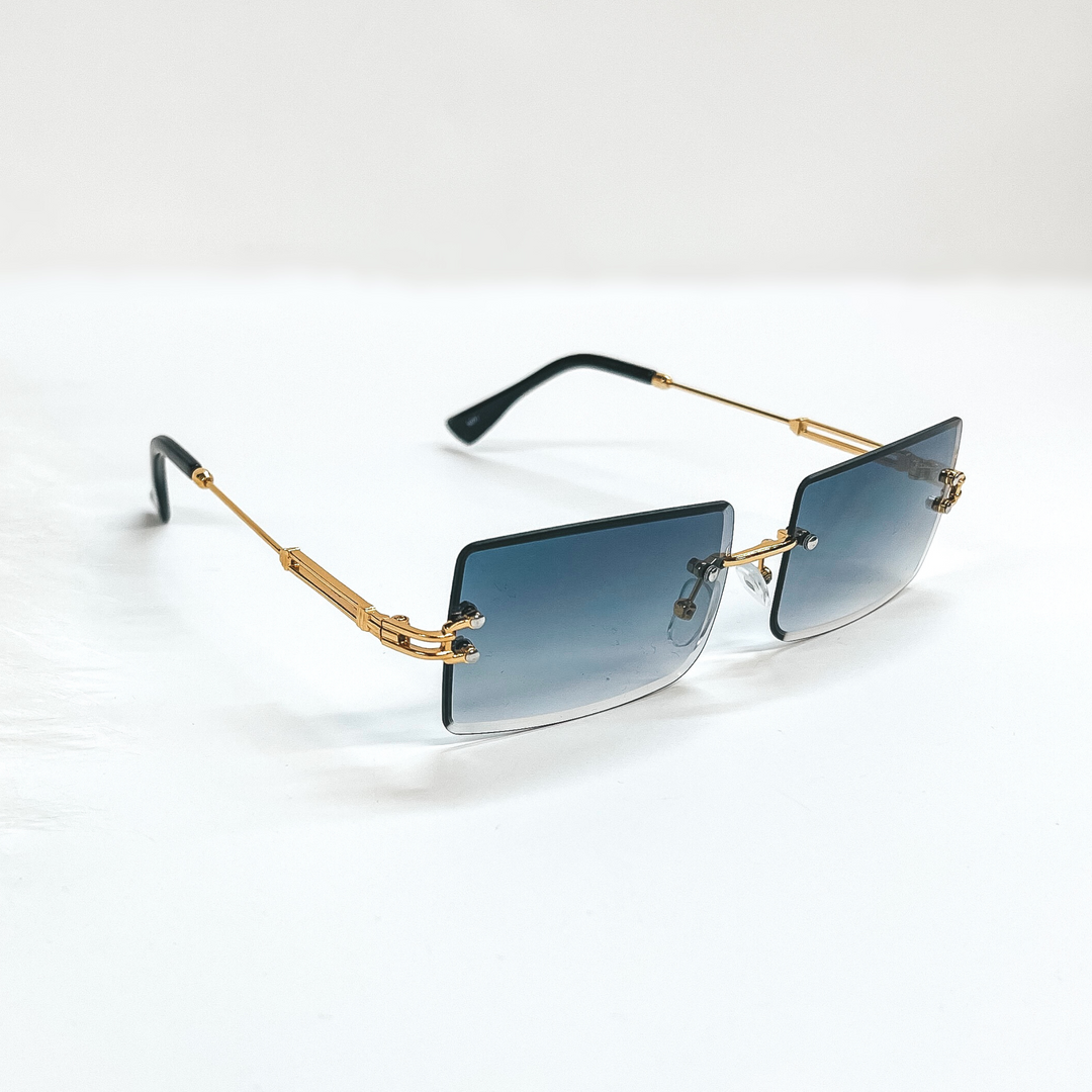 This is a black/dark grey pair of sunglasses, the lenses are black/dark grey  with no frame and they have  gold connectors. The ear pieces are black. These sunglasses are taken  on a white background with a piece of white fur in the side as decor.