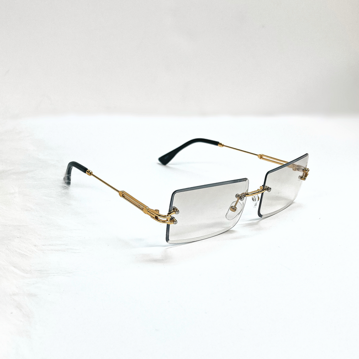 This is a clear grey/brown pair of sunglasses, the lenses are clear brown/grey  with no frame and they have  gold connectors. The ear pieces are black. These sunglasses are taken  on a white background with a piece of white fur in the side as decor.