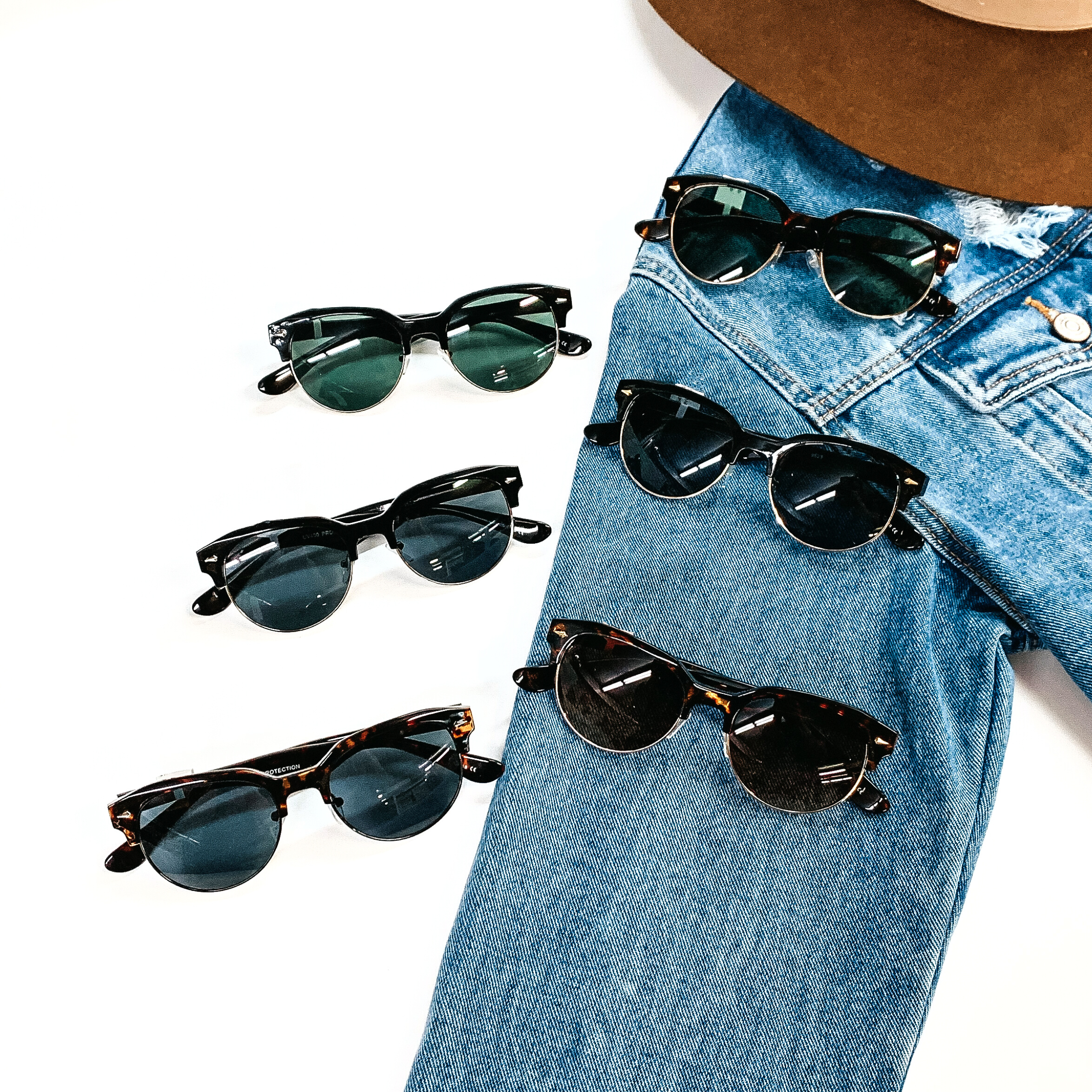There are six pairs of browline sunglasses in different colors/print such as  tortouise print and black with different color lenses as well. These sunglasses are  taken on a white background and jean jacket sleeve with a dark brown felt hat on the  top as decor.