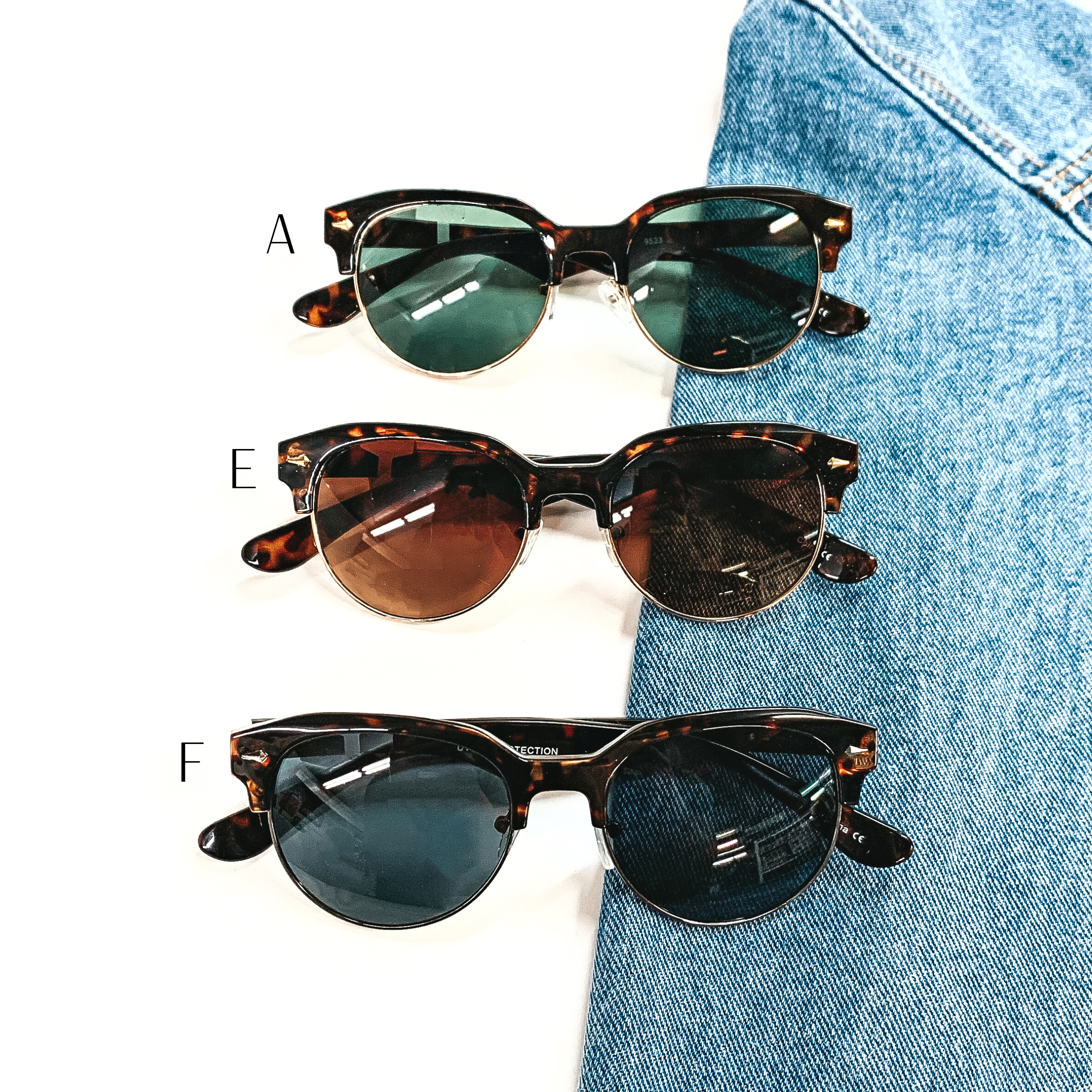 There are three pairs of browline style sunglasses in tortouise print for the frame  and different colors of lenses. Style A has a tortouise print frame, dark green  lense with a gold tone outline. Style E has a tortuoise print frame, brown lense with a  gold tone outline. Style F has a tortouise print frame with a black/dark grey lense  with a gunmetal/black outline. These three pairs of sunglasses are taken on a white  background and on a jean jacket sleeve.